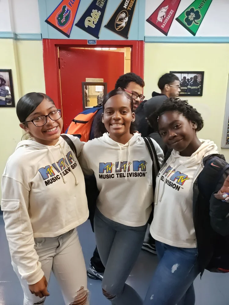 Three smiling students wearing matching hoodies in school hallway