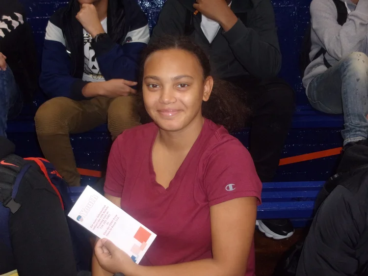 Student smiling in bleachers holding a school event pamphlet