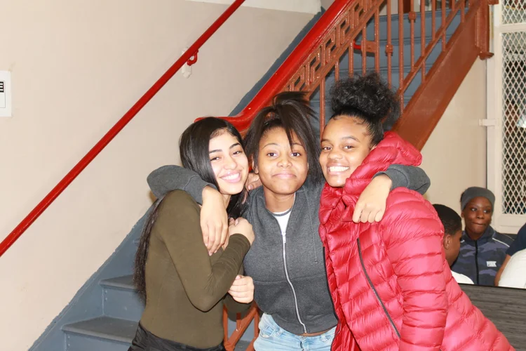Three smiling students posing together near school staircase