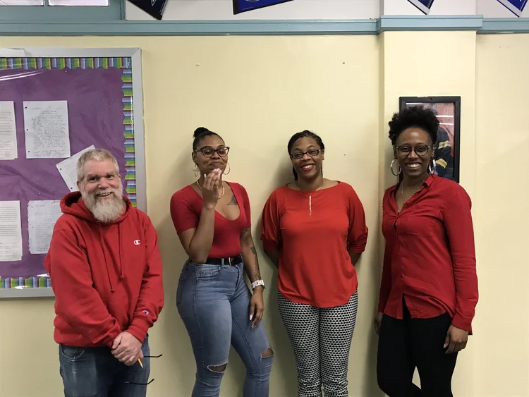 Four staff members wearing red pose together in a classroom