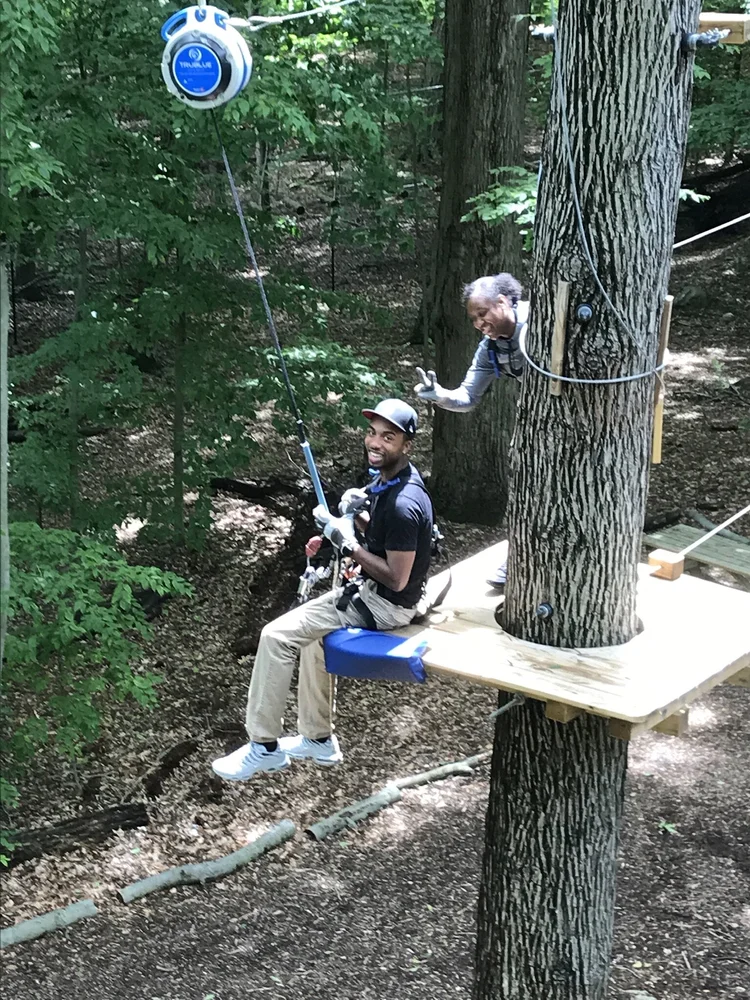 Student smiling while zip lining through a forest course