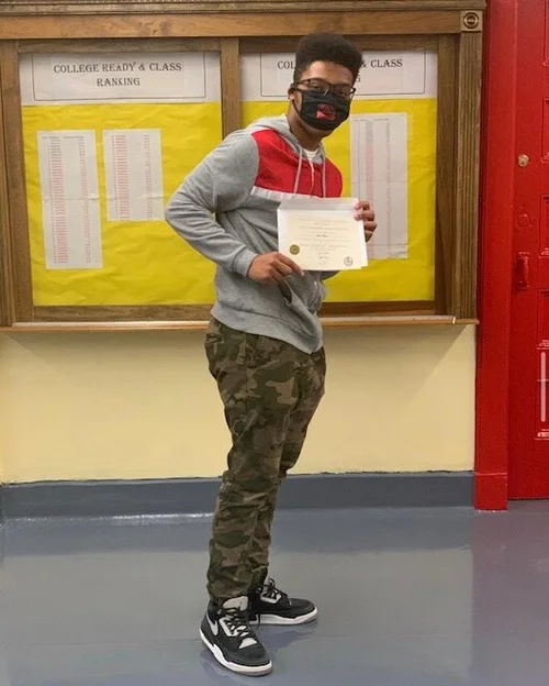 Student holding certificate near college ready class ranking board
