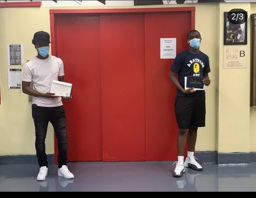 Two students holding certificates while wearing masks indoors