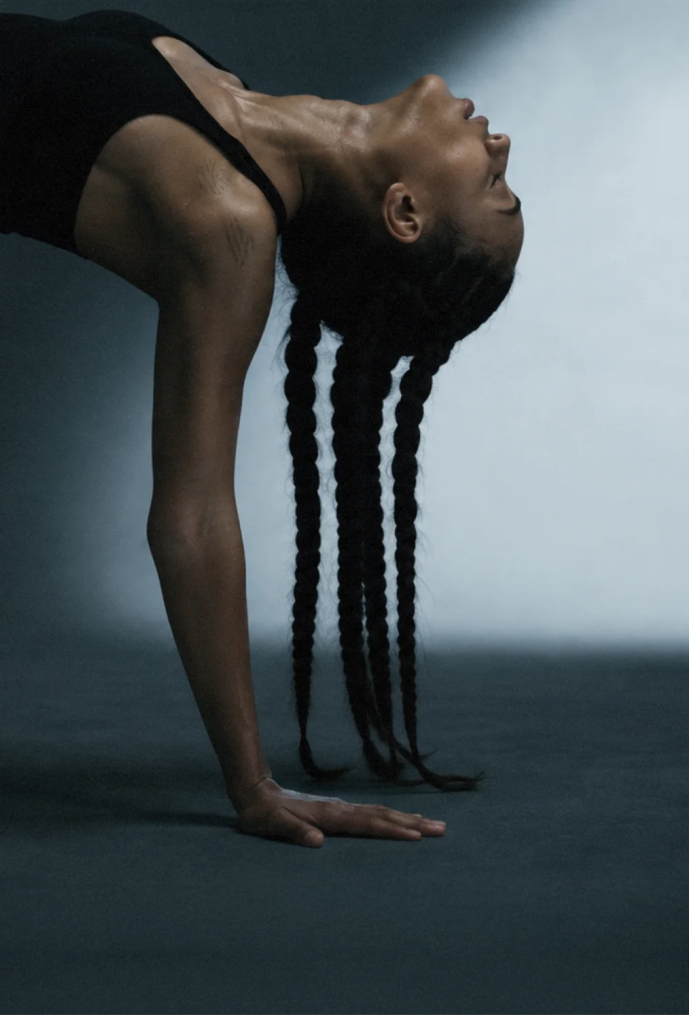 Person in black outfit bending backward on hands with long braided hair hanging down.
