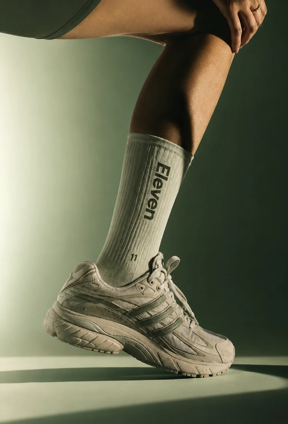 Person's leg wearing white sneaker and mid-calf sock with 'Eleven' text in soft light.