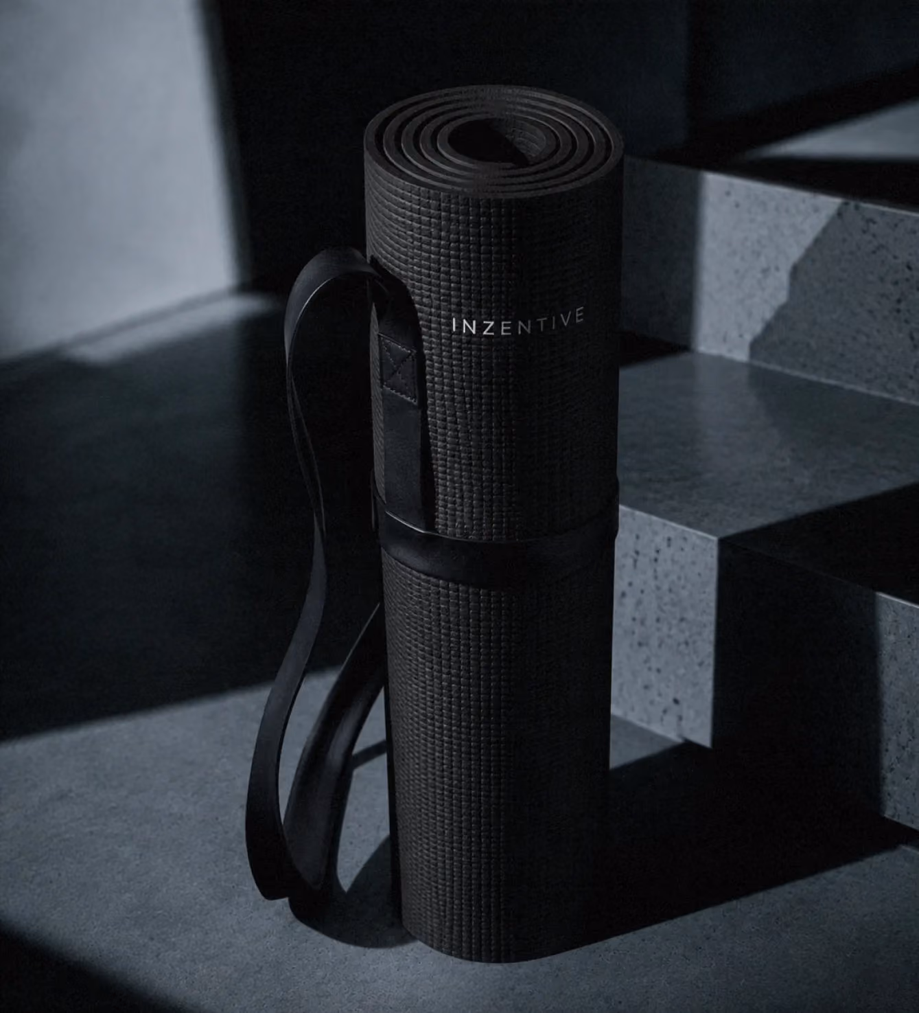 Rolled black yoga mat with the Inzentive logo, leaning against concrete steps.