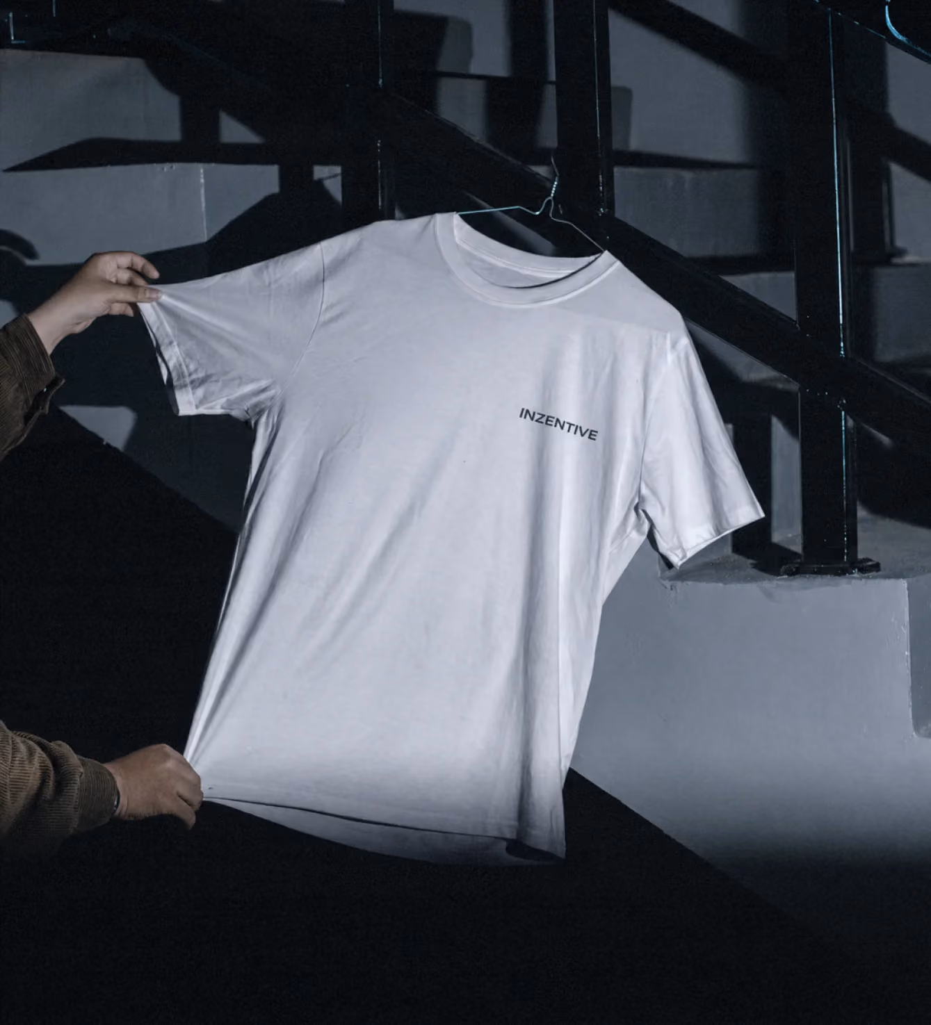 White Inzentive-branded t-shirt held up on a hanger near a staircase.