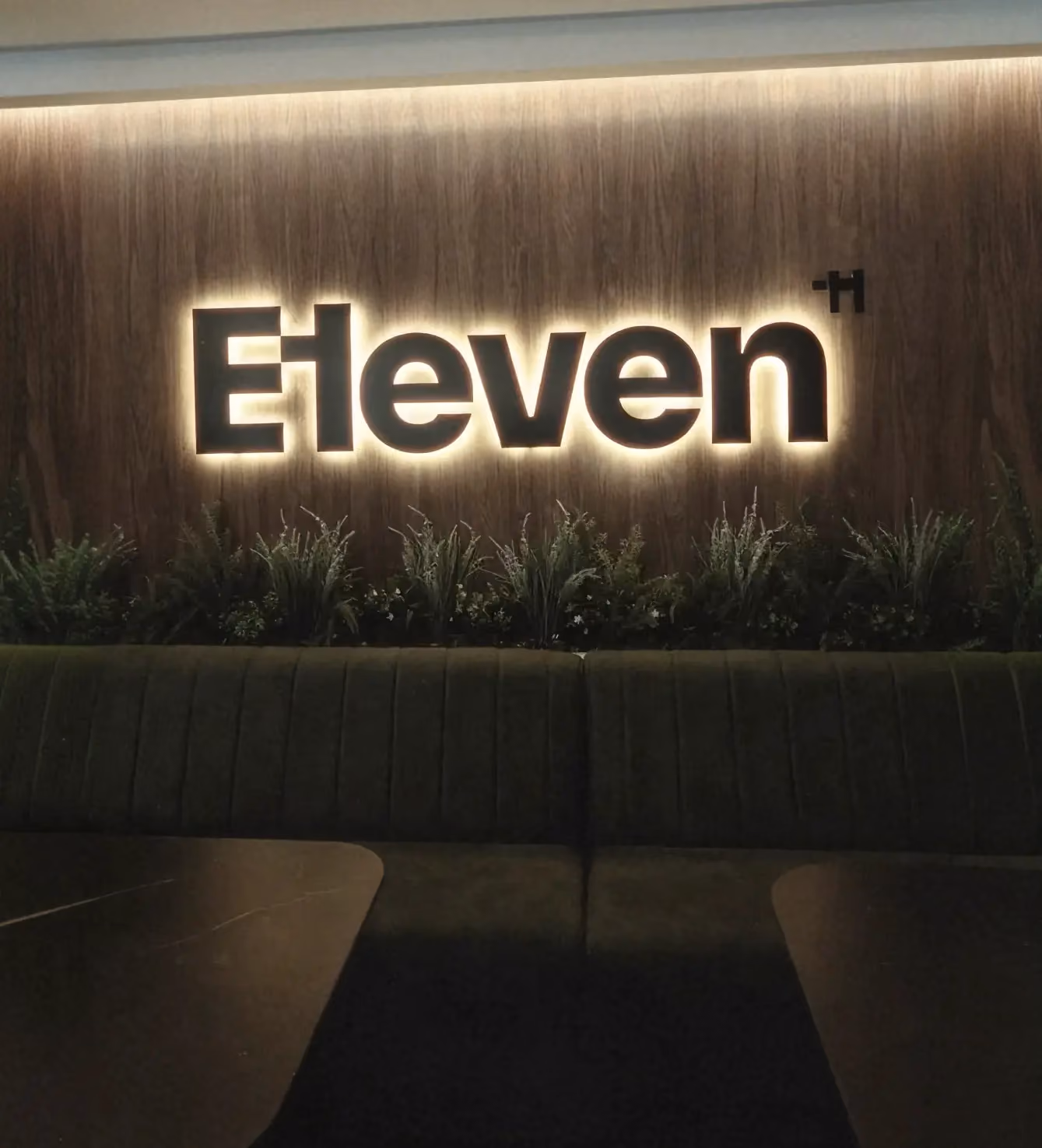 Backlit "Eleven" logo sign on a wood-paneled wall above a green booth seating area.