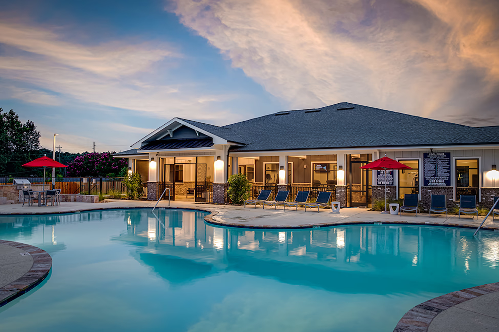 Outdoor swimming pool in front of a residential clubhouse at sunset.