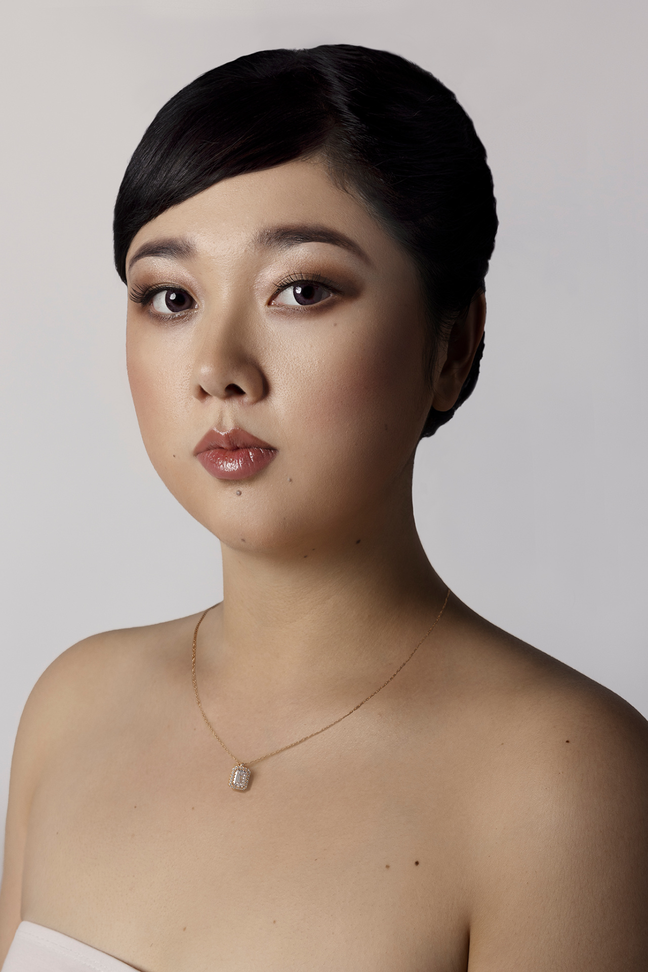 Yuwei, cantante lirica, ritratto beauty ravvicinato con capelli raccolti e collana a pendente dorato, fotografia fine art per book professionale di Claudia Spaziani a Bologna.