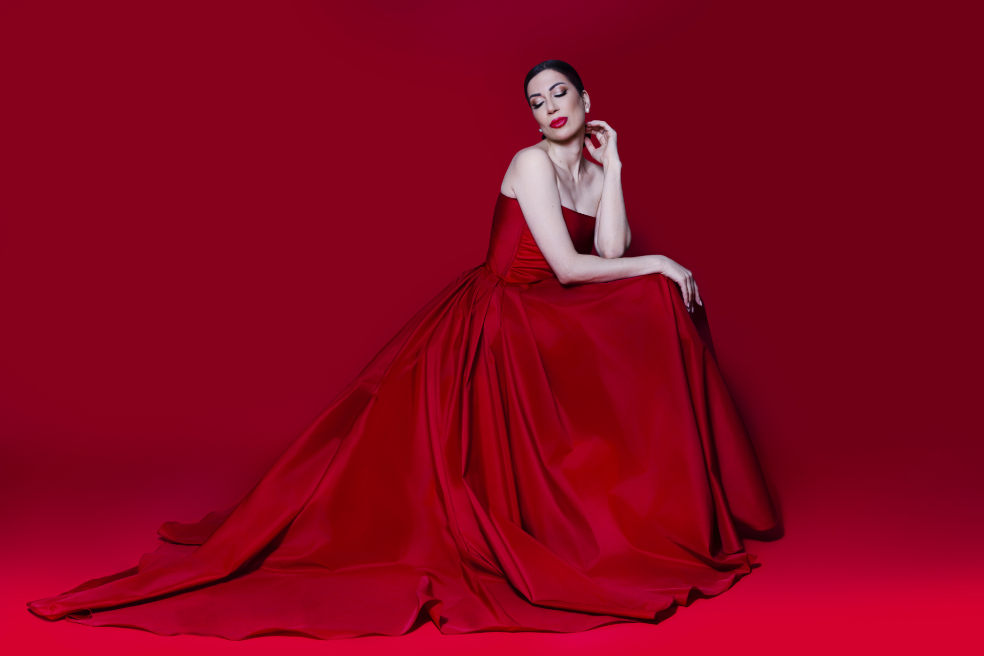 Soprano in abito rosso con strascico adagiata a terra con occhi chiusi e posa raccolta, ritratto fine art per book professionale di Claudia Spaziani a Castel Guelfo, Bologna.