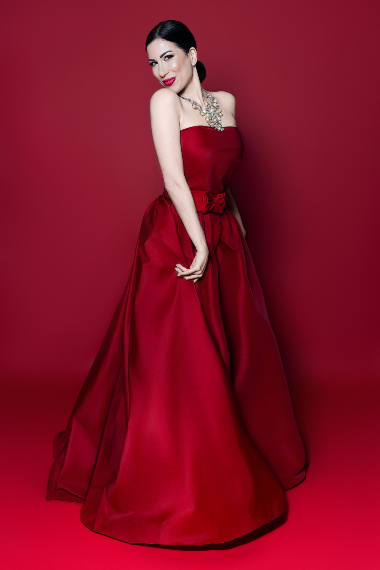 Rosy, cantante lirica, in abito da ballo rosso con corsetto a cuore e collana di perle, ritratto elegante per book professionale di Claudia Spaziani a Bologna.