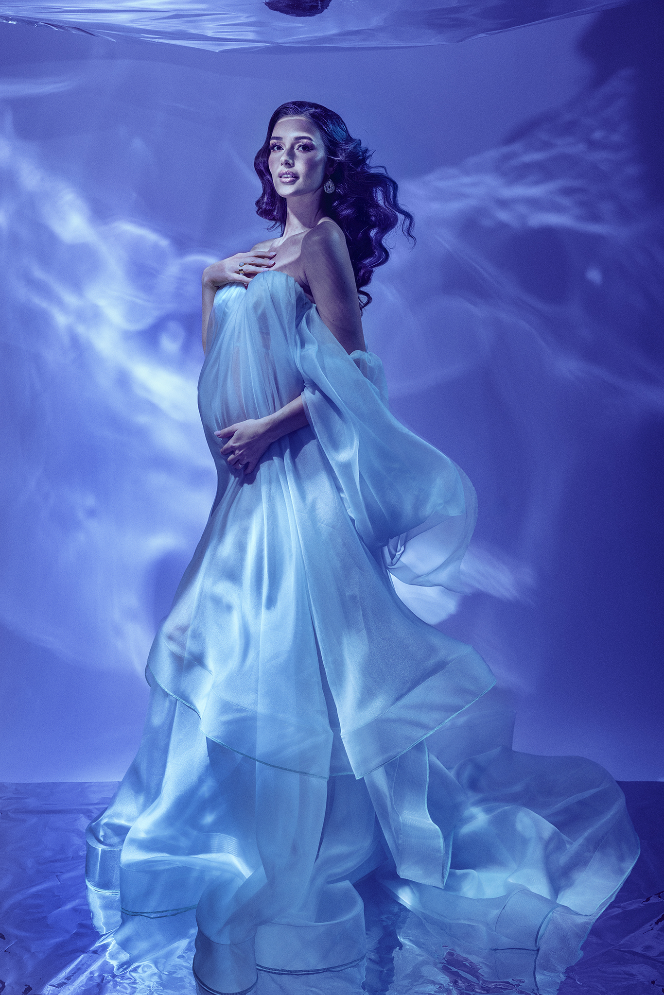 OPERA by Claudia Spaziani – produzione fotografica fine art di maternità esclusiva a Bologna: donna incinta in abito organza azzurra con luci acquatiche, un mondo costruito su misura e mai ripetuto