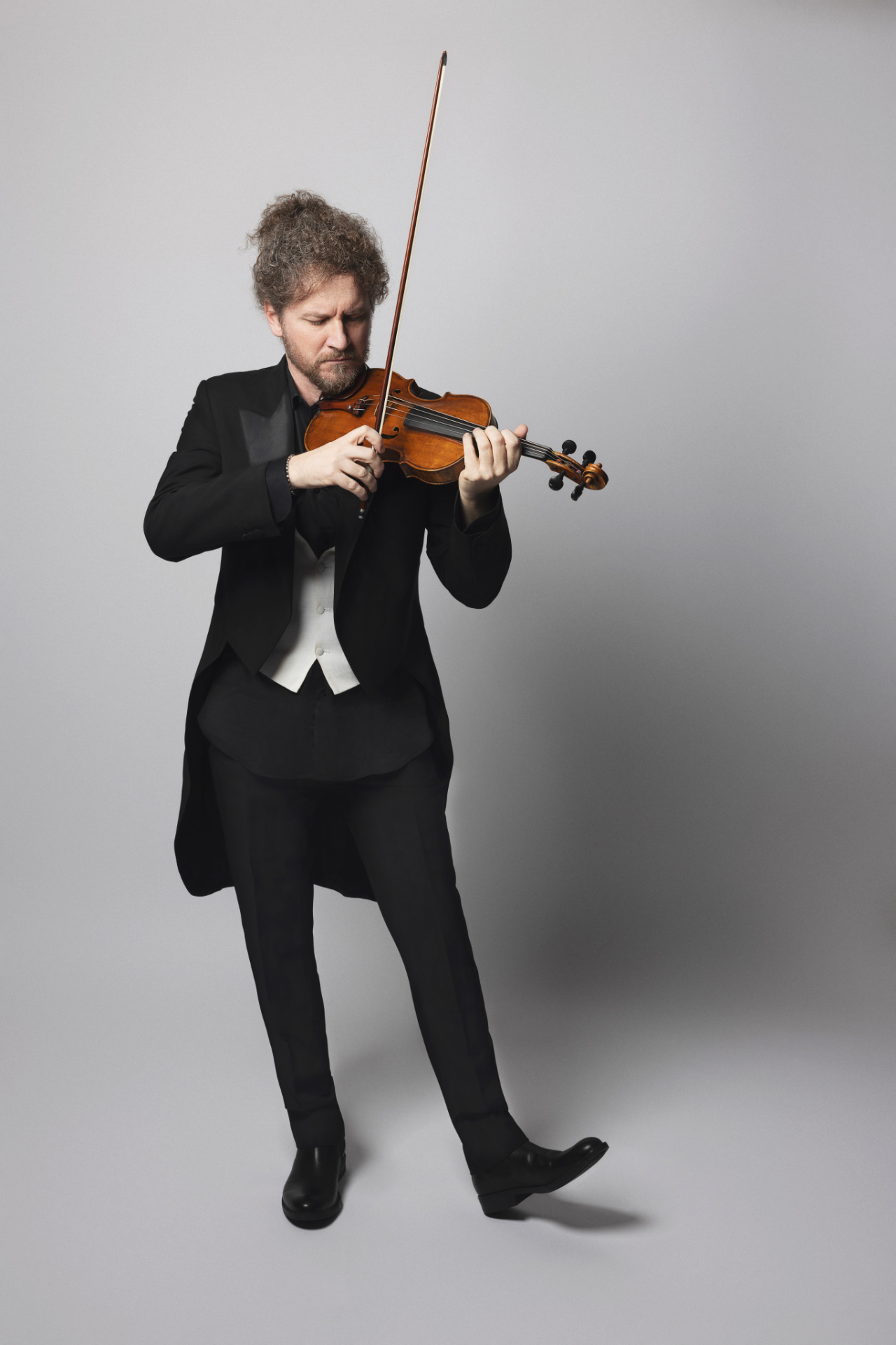 Violinista in frac da concerto mentre suona il violino a figura intera, posa dinamica su sfondo grigio, ritratto per book di Claudia Spaziani a Bologna.