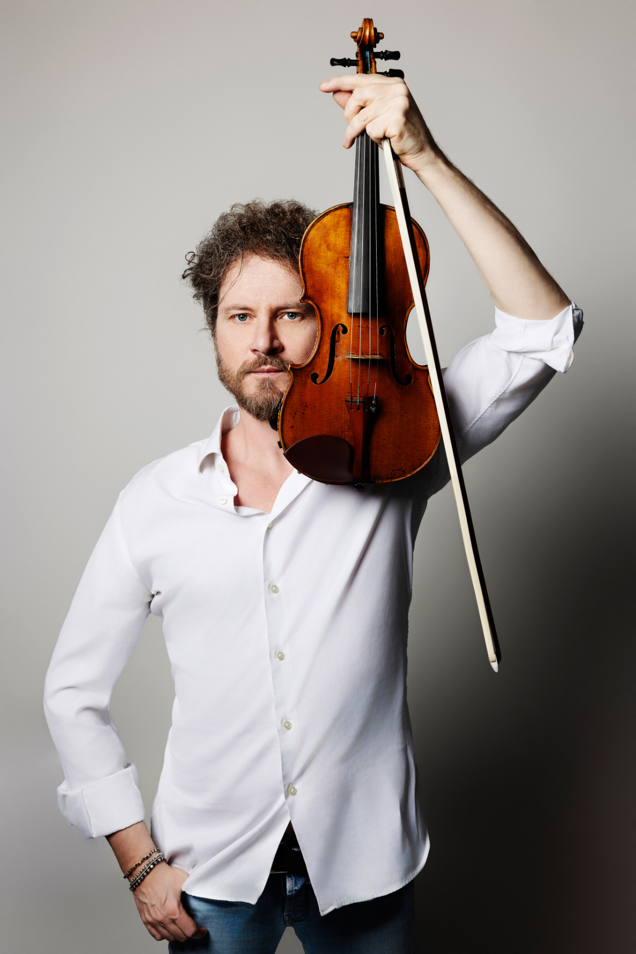 Marco, violinista, in camicia bianca con violino sollevato accanto al viso e sguardo intenso in camera, ritratto fine art per book professionale di Claudia Spaziani a Bologna.