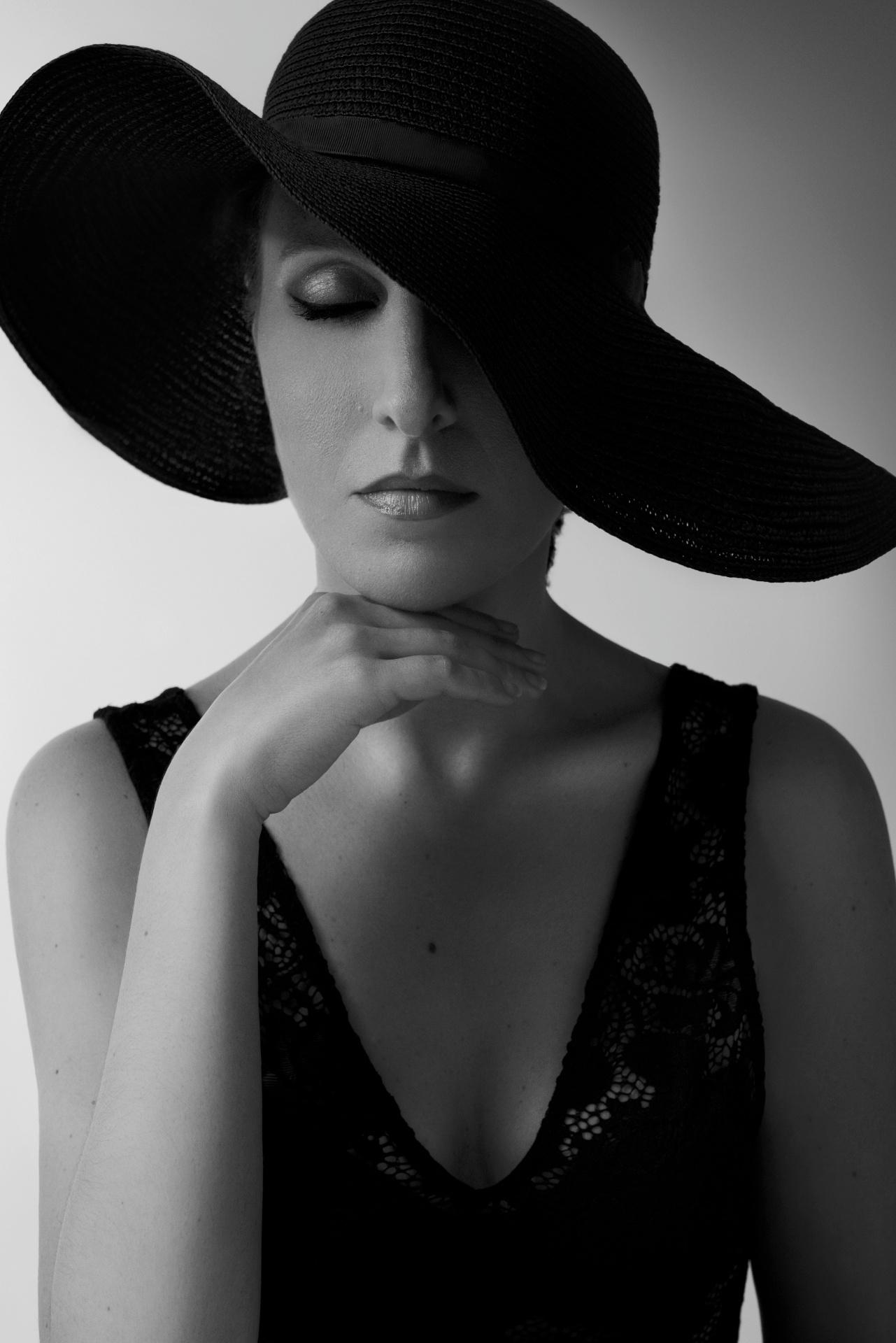 Cantante lirica in bianco e nero con cappello a tesa larga nero e abito in pizzo, mano al collo in posa raccolta, ritratto fine art per book di Claudia Spaziani a Bologna.