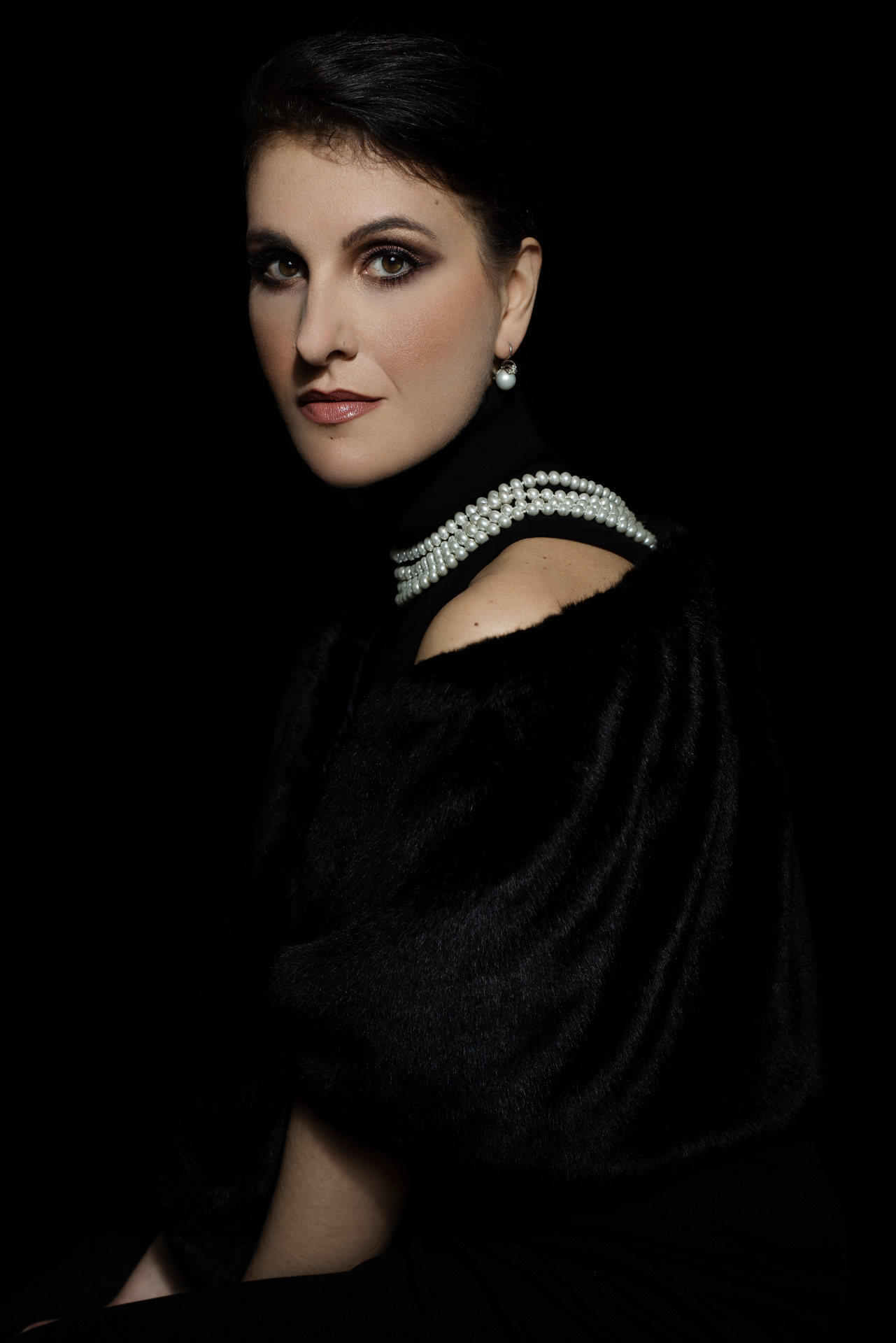 Luisa, soprano, con mantella di velluto nero e collana di perle sulla spalla, sguardo intenso su sfondo scuro, ritratto per book professionale di Claudia Spaziani a Bologna.