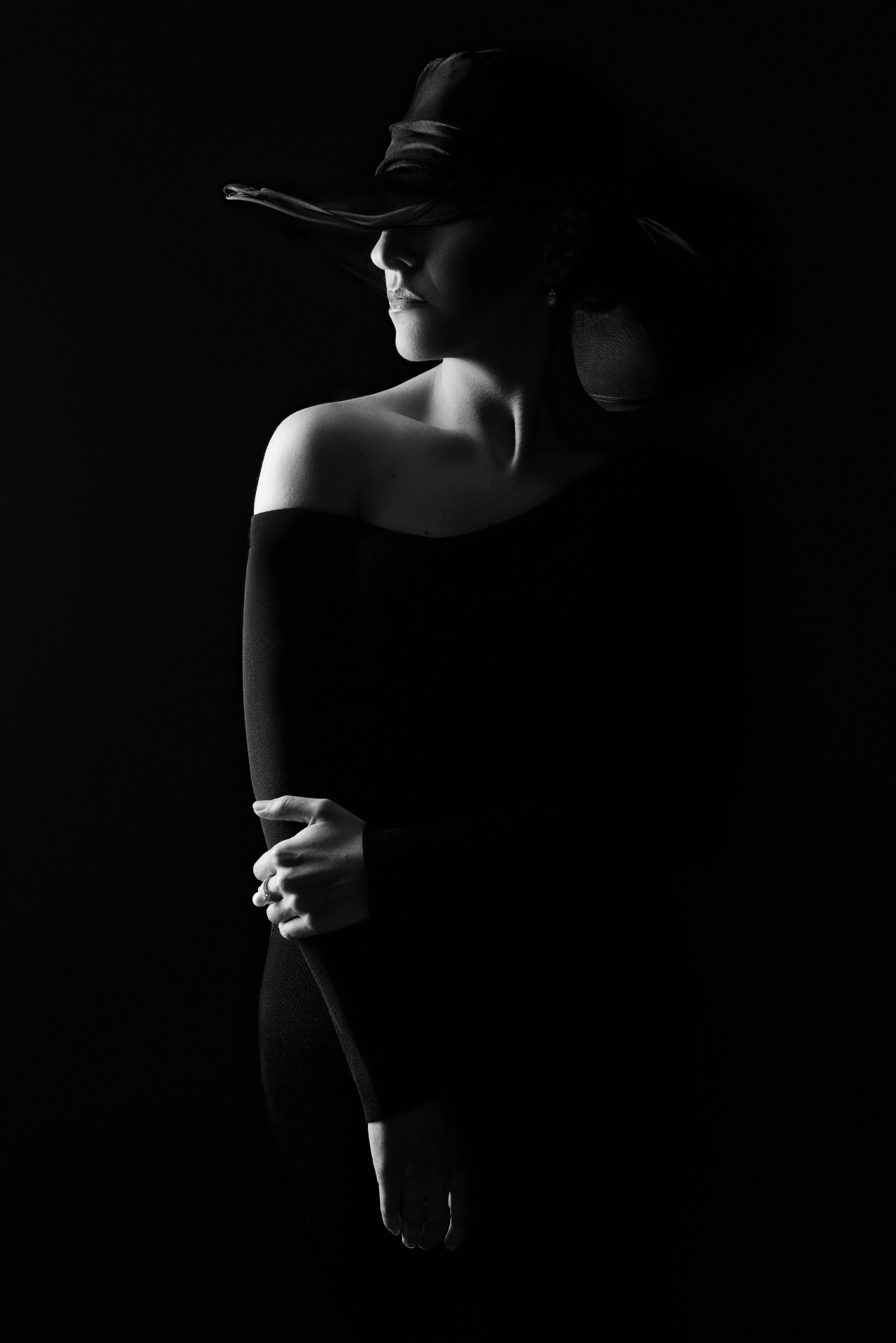Soprano in bianco e nero con copricapo scuro che vela il viso, posa teatrale su sfondo nero, ritratto fine art per book di cantante lirica di Claudia Spaziani a Bologna.