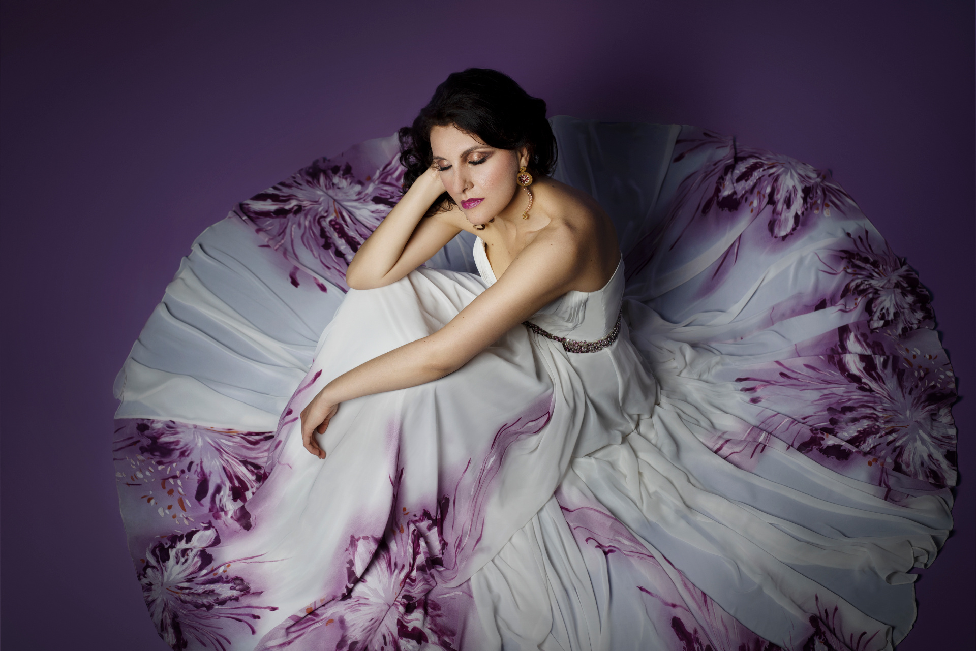 Luisa, soprano, adagiata in abito bianco a fiori viola dispiegato su sfondo viola, ritratto fine art onirico per book professionale di Claudia Spaziani a Bologna.