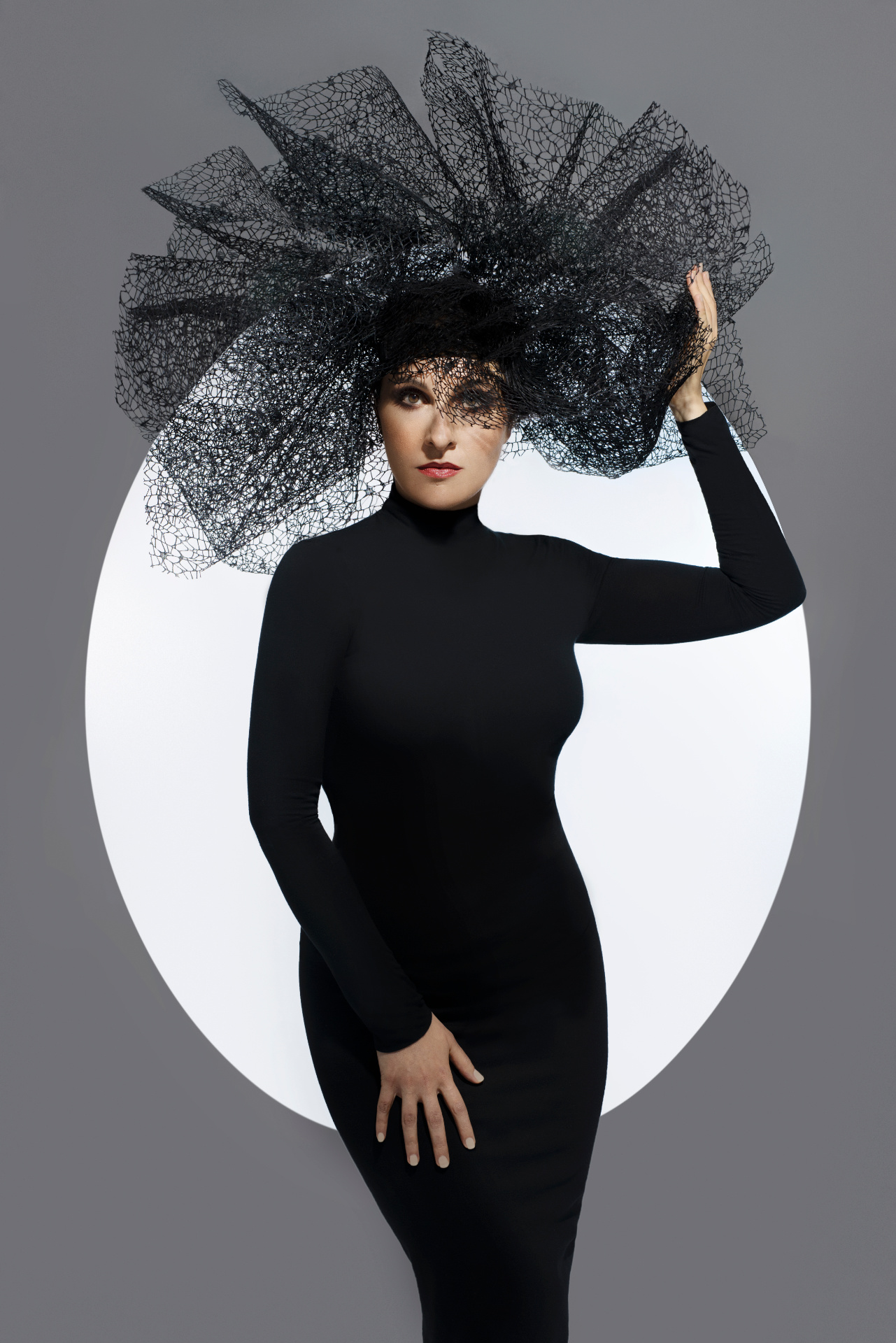 Luisa, cantante lirica, in abito nero con copricapo in tulle strutturato davanti a cerchio luminoso, ritratto fine art per book professionale di Claudia Spaziani a Bologna.