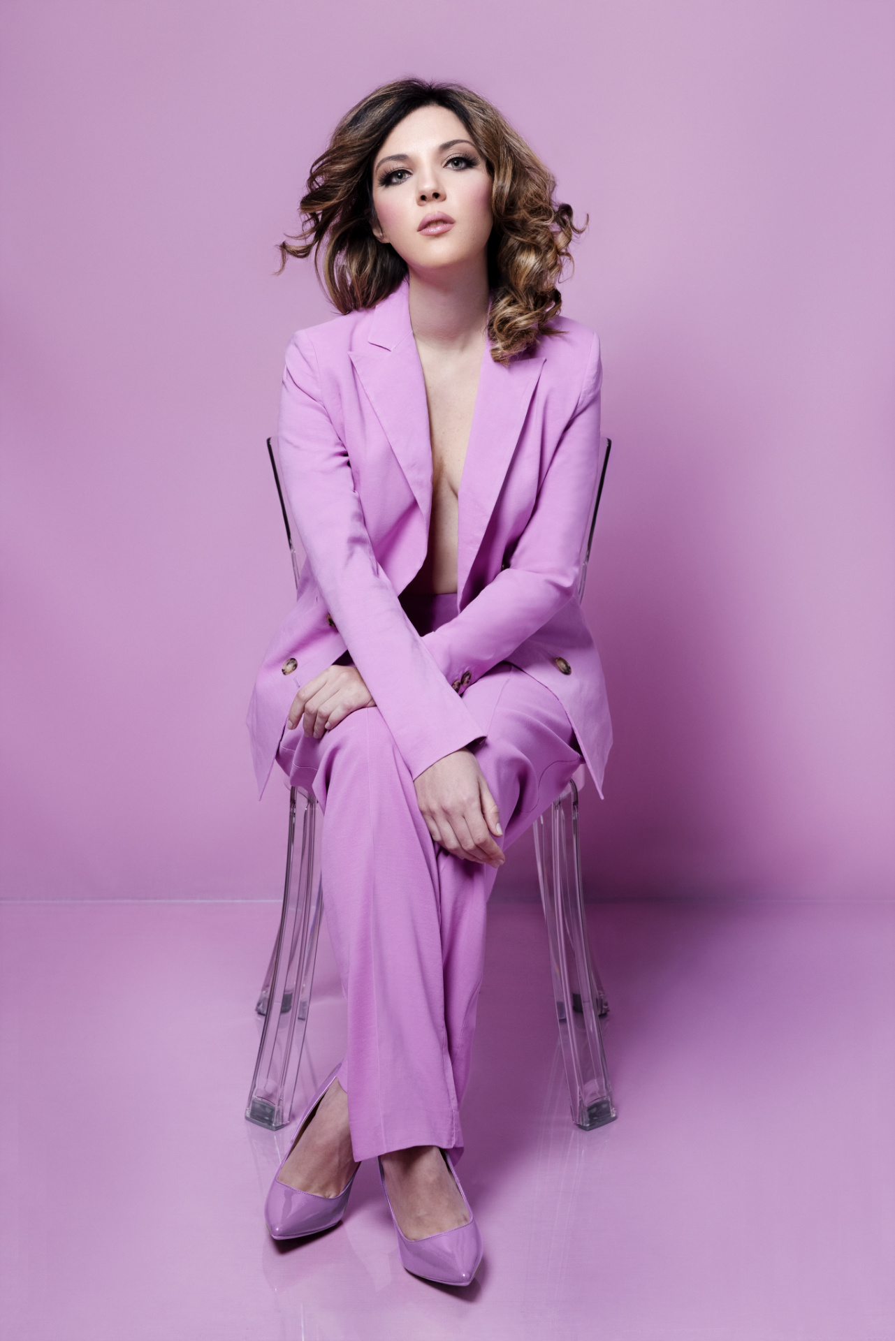 Ritratto professionale di soprano in tailleur lilla su sedia trasparente con sguardo intenso, fotografia per book artistico di Claudia Spaziani a Bologna.