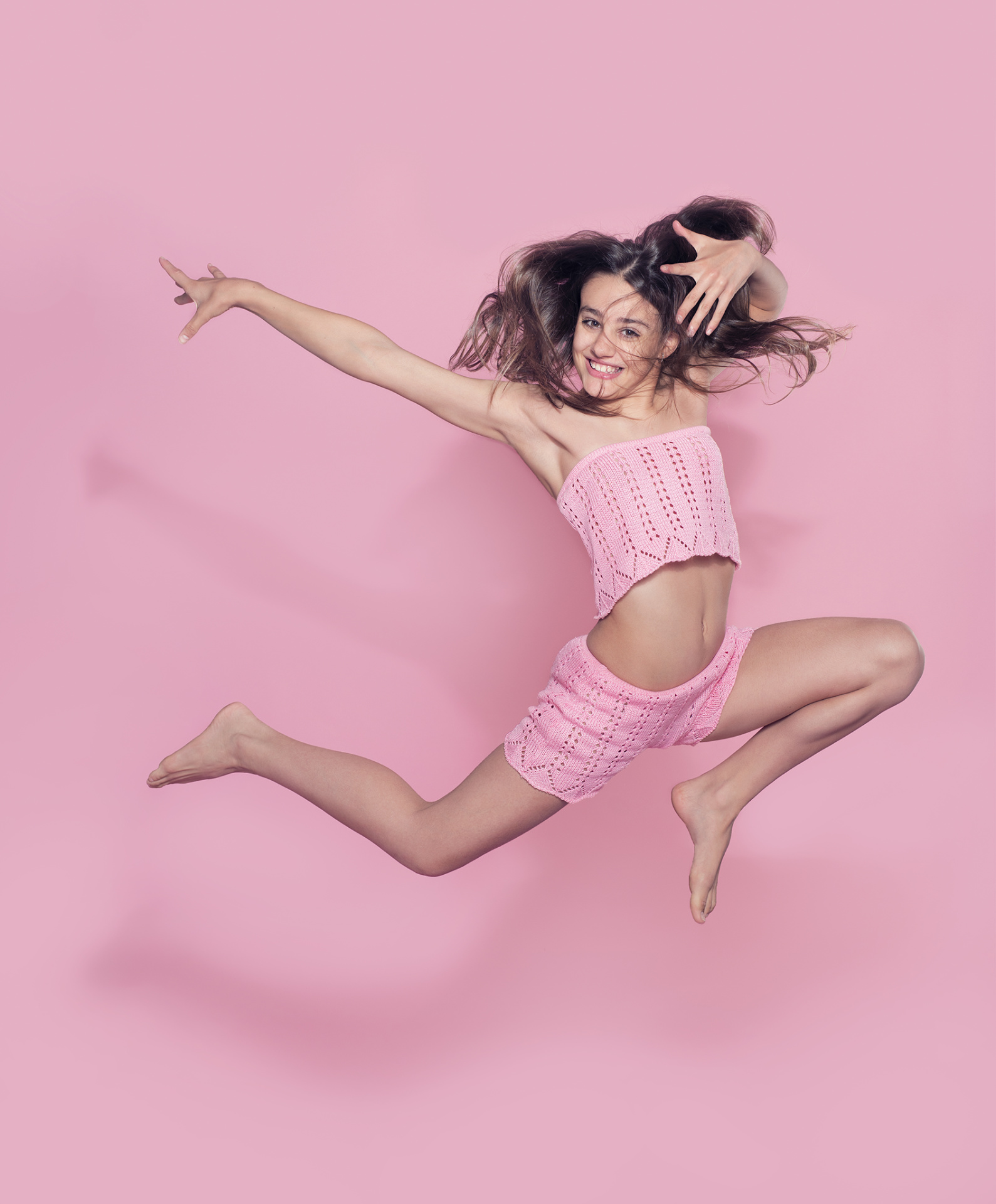 Ragazza in outfit rosa che salta con capelli al vento e sorriso esplosivo, ritratto fine art vivace di Claudia Spaziani nel suo studio a Bologna.