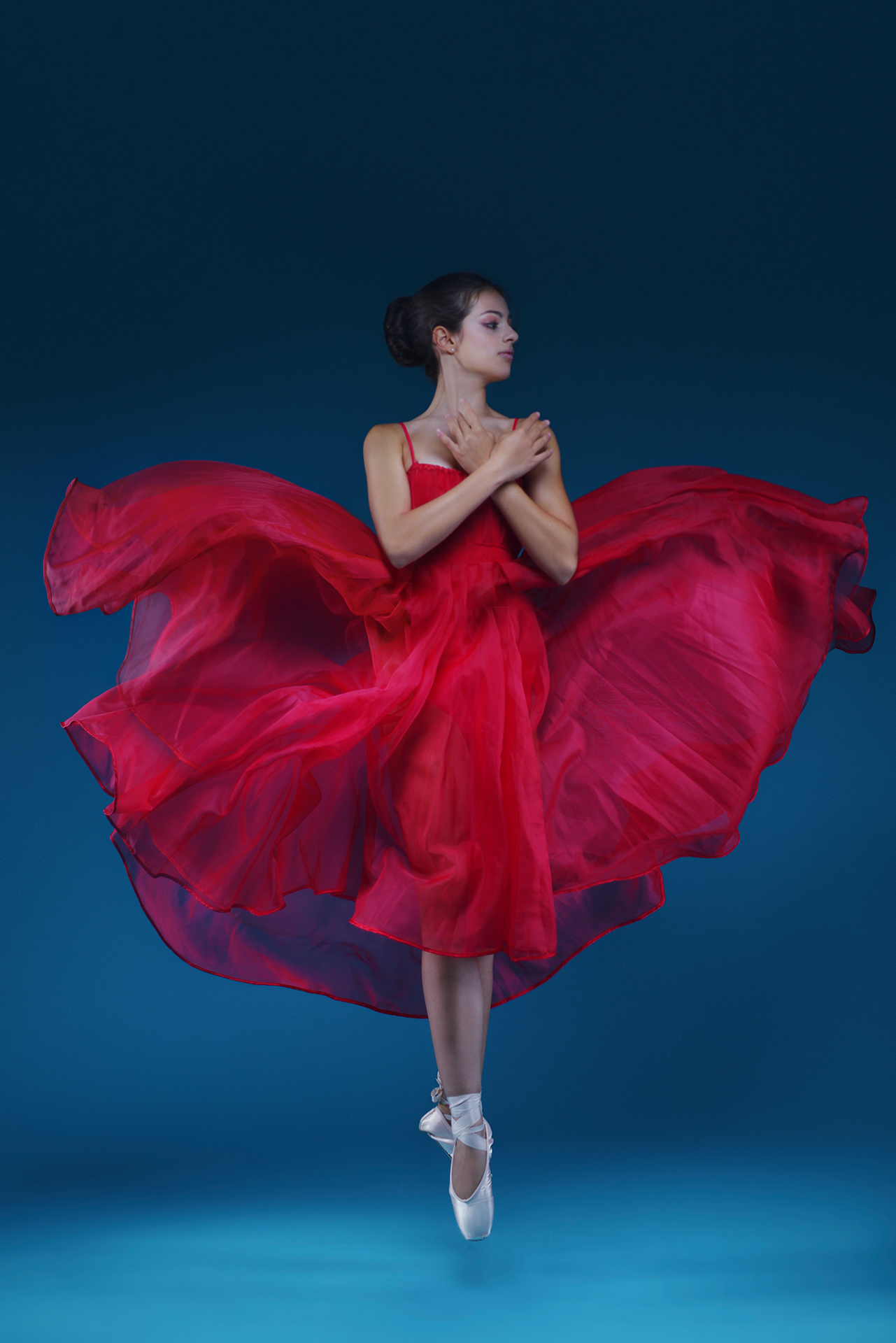 Ballerina in abito rosso in volo con tessuto svolazzante e mani sul petto, ritratto fine art di Claudia Spaziani nel suo studio a Bologna.