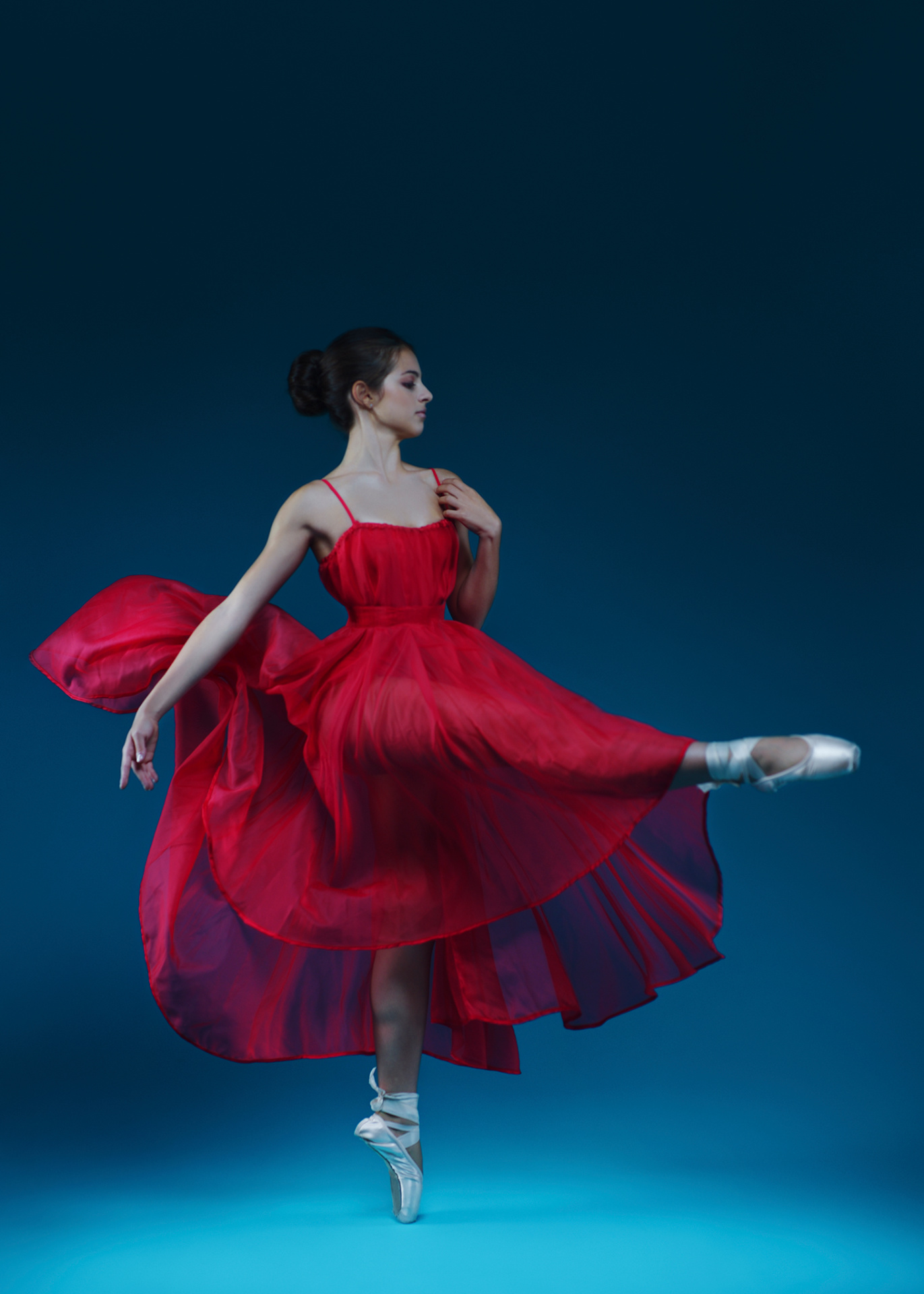 Ballerina in abito rosso fluente danza in punta su sfondo blu scuro, ritratto fine art dinamico e poetico di Claudia Spaziani a Bologna.