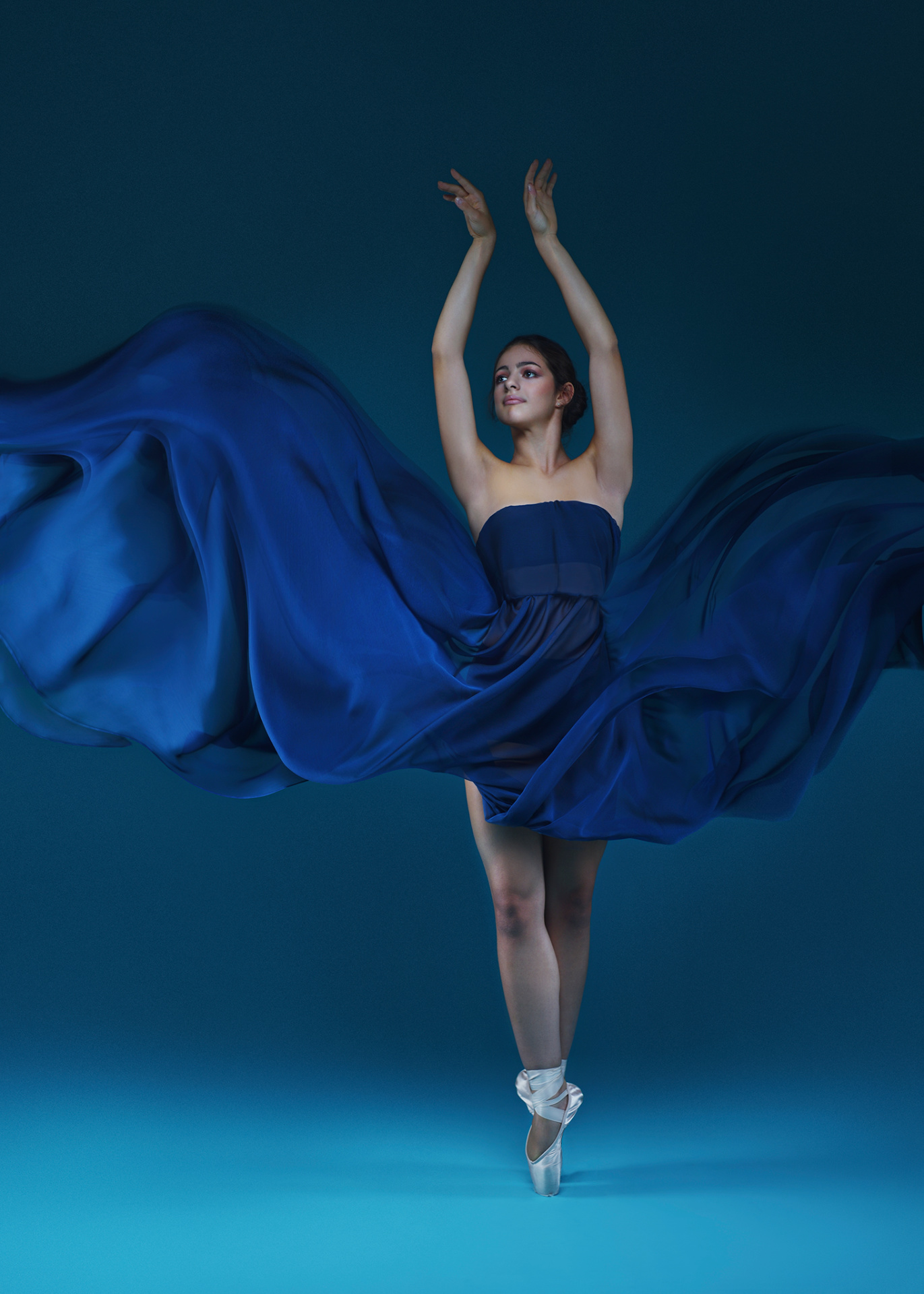 Ballerina in abito blu notte con tessuto in movimento e braccia alzate in punta, ritratto fine art di Claudia Spaziani a Castel Guelfo, Bologna.