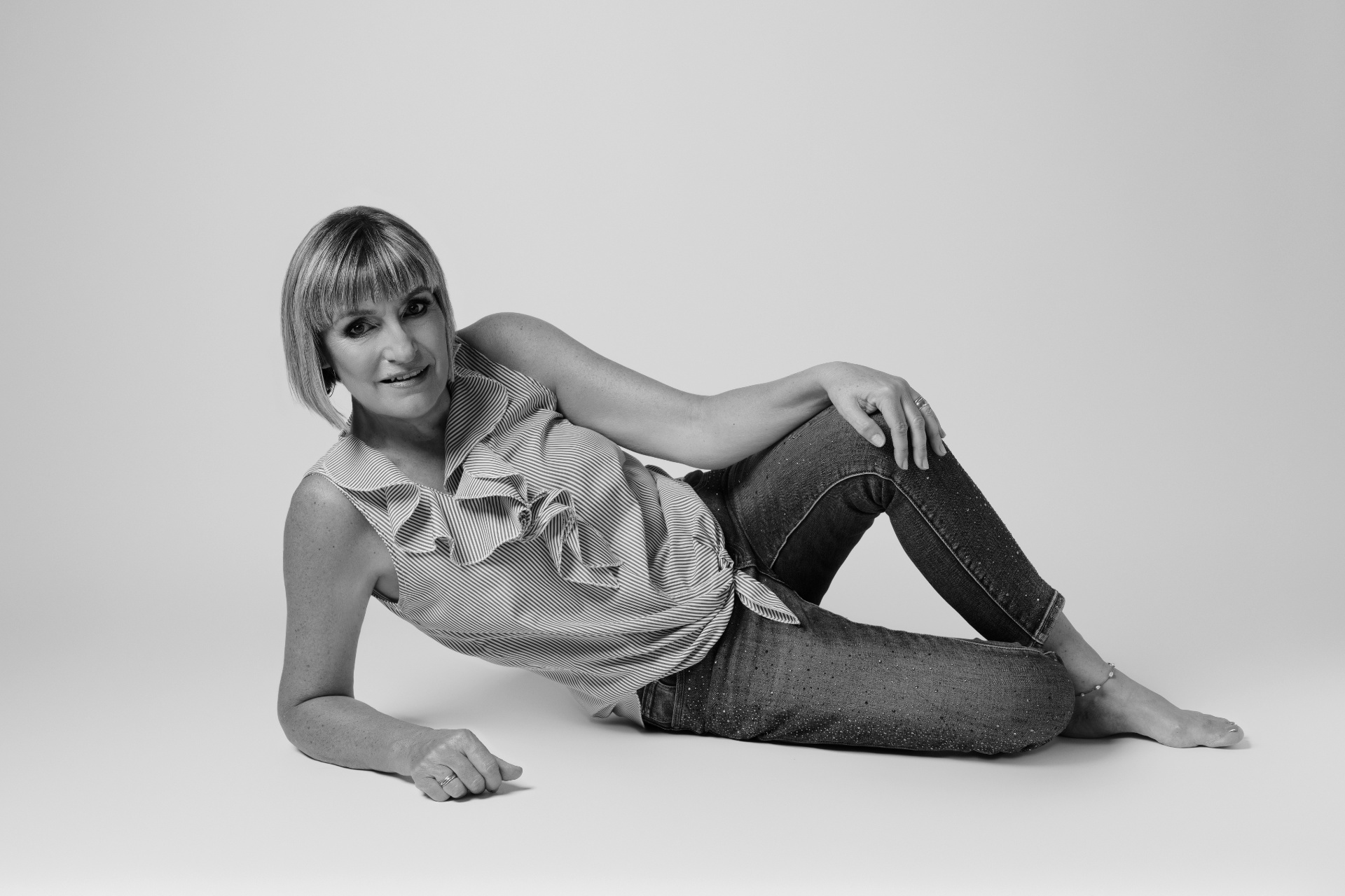 itratto fine art in bianco e nero di una donna sdraiata con top a righe senza maniche e jeans aderenti. Posa rilassata e sfondo minimalista. Fotografia glamour realizzata da Claudia Spaziani nel suo studio a Bologna.
