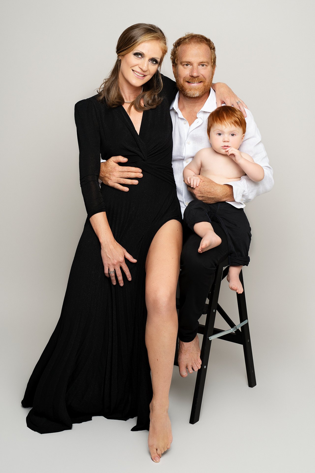Fotografia fine art di madre, padre e figlio, scattata da Claudia Spaziani a Bologna. Lei in abito nero, lui in camicia bianca e pantaloni neri, il bambino in braccio, tutti scalzi.