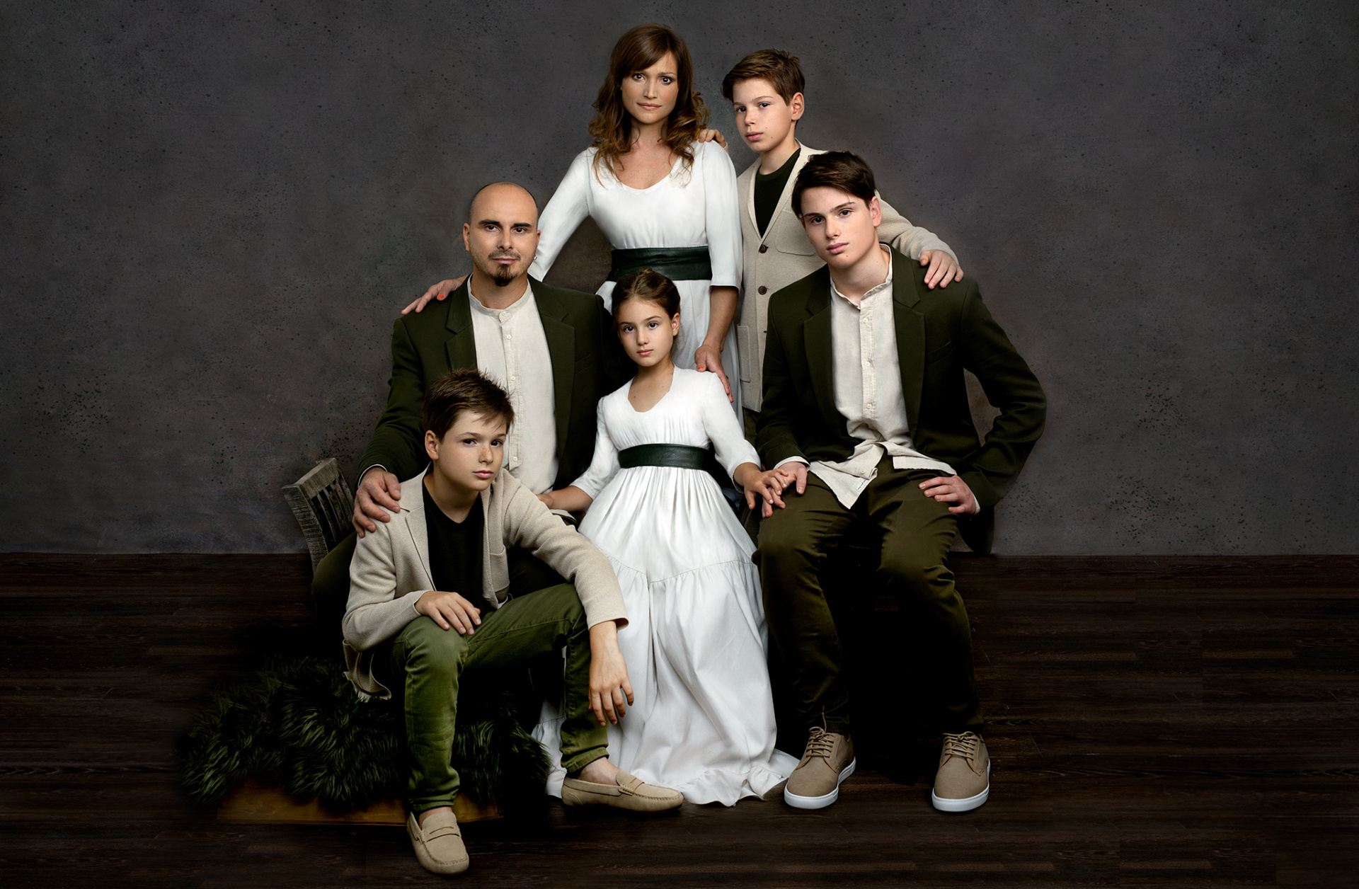 Ritratto di famiglia in studio su fondale grigio: genitori e quattro figli in abiti coordinati nei toni del verde oliva, bianco e beige. Claudia Spaziani, Bologna.