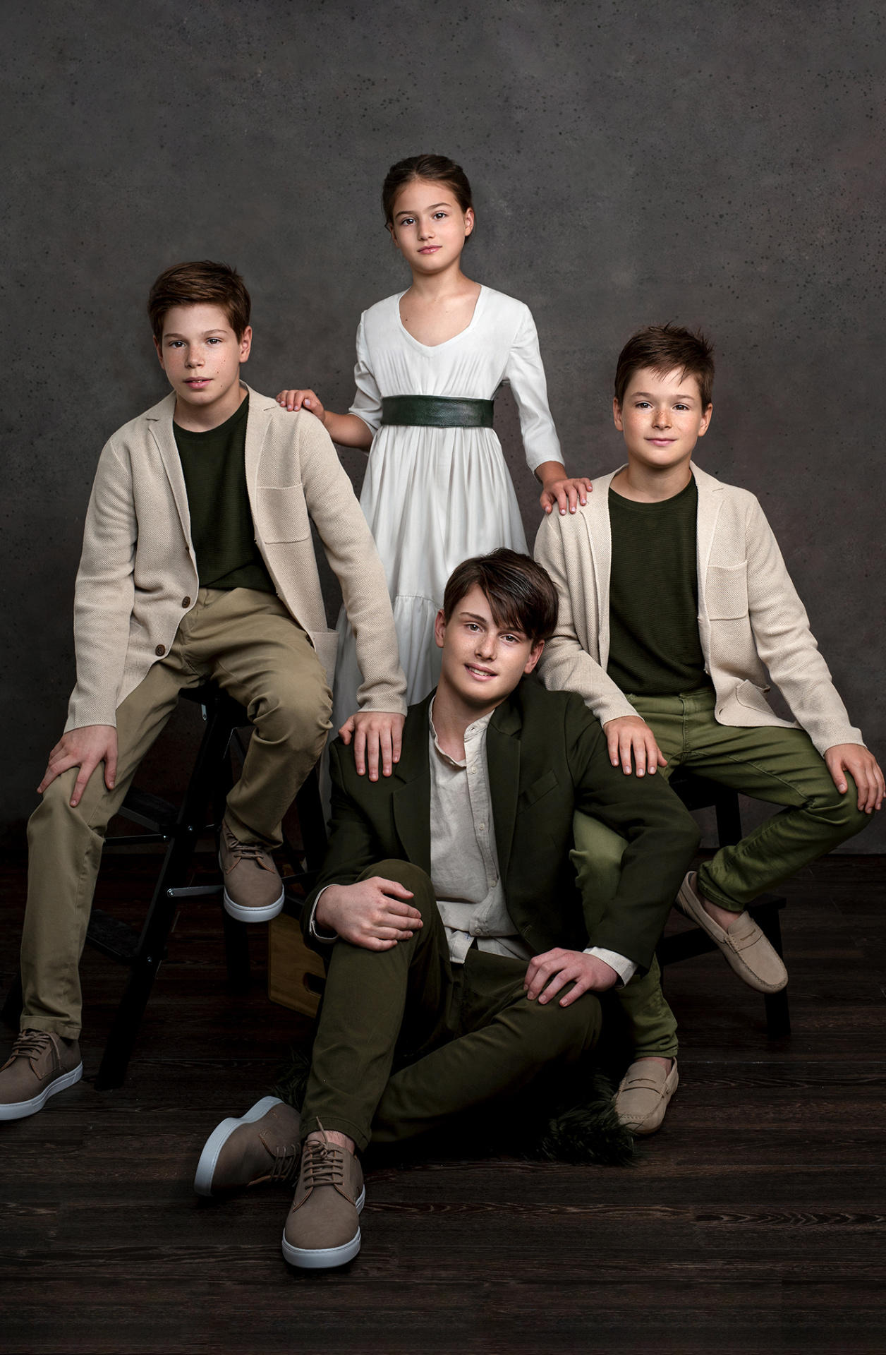 Fotografia fine art di quattro fratelli in abiti eleganti, scattata da Claudia Spaziani nel suo studio a Bologna. Composizione simmetrica con abiti verde oliva e beige su sfondo scuro.
