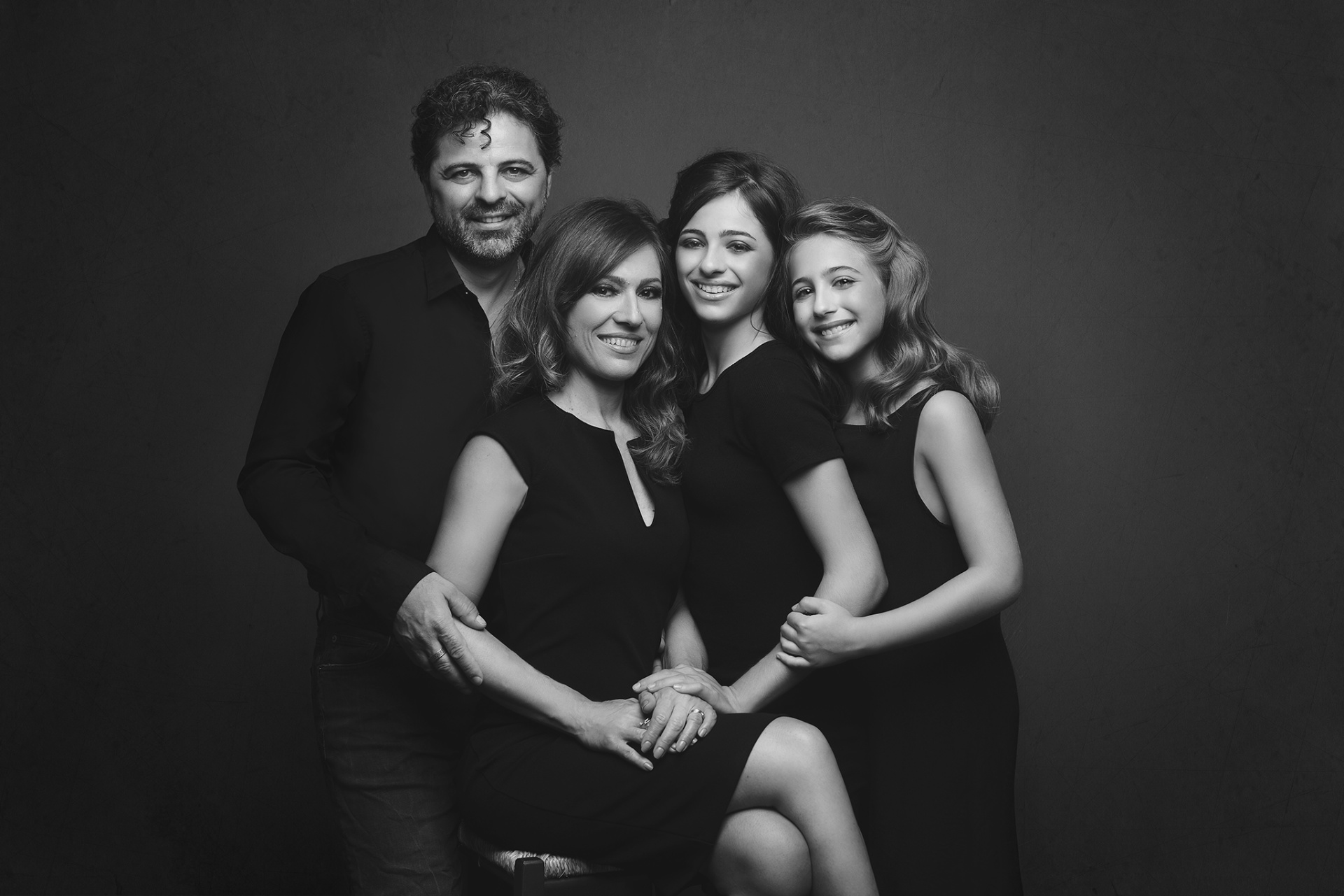 Ritratto artistico in bianco e nero di famiglia con due adulti e due giovani, realizzato da Claudia Spaziani nel suo studio a Bologna. Tutti in abiti neri, in posa affettuosa su sfondo scuro.
