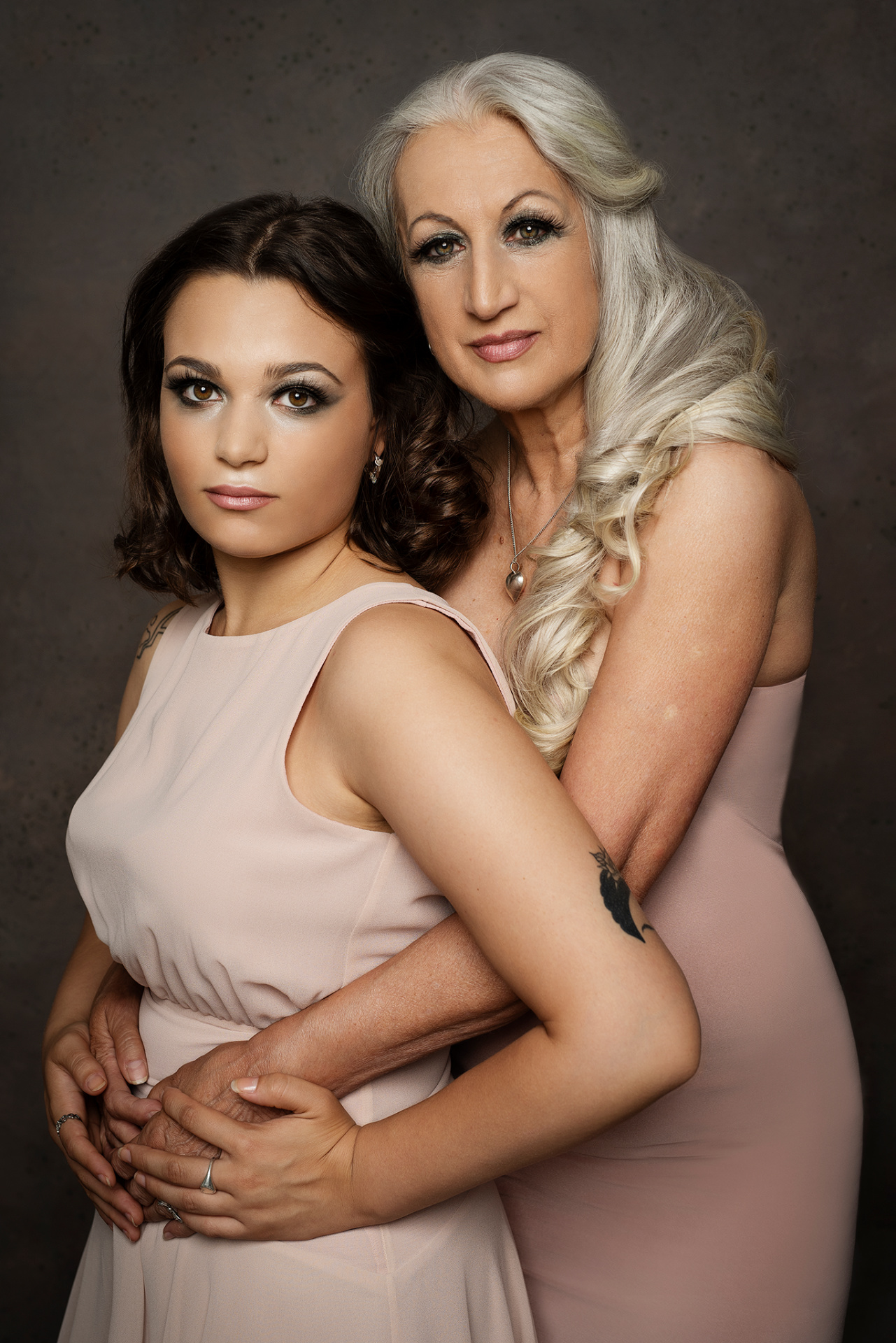 Fotografia fine art di madre e figlia in abiti rosa cipria, scattata da Claudia Spaziani nel suo studio fotografico a Bologna. Posa affettuosa su sfondo scuro, con capelli sciolti e trucco elegante.