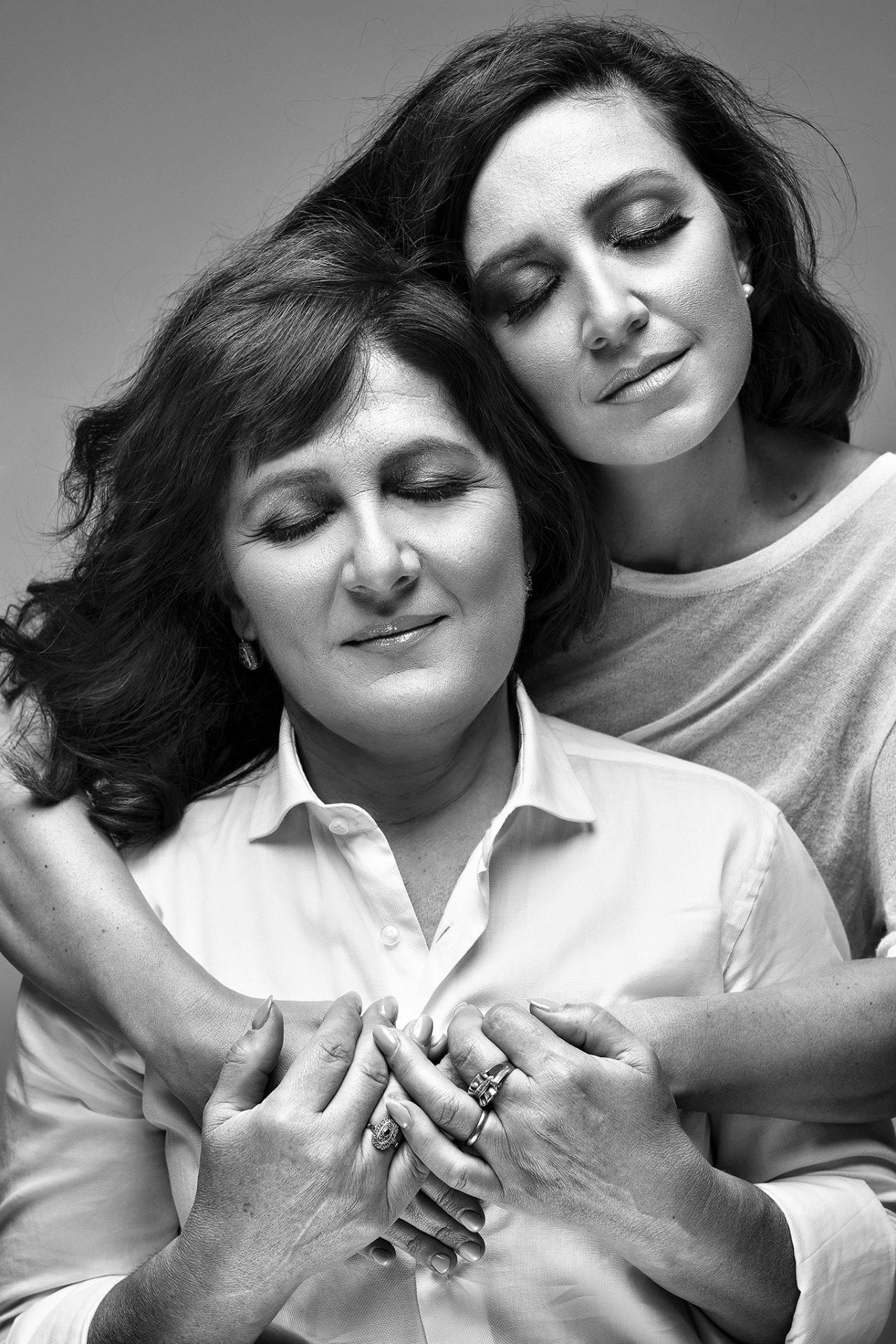 Ritratto artistico in bianco e nero di madre e figlia abbracciate, con occhi chiusi e mani intrecciate, realizzato da Claudia Spaziani nel suo studio fotografico a Bologna. Espressione serena e gesti affettuosi.
