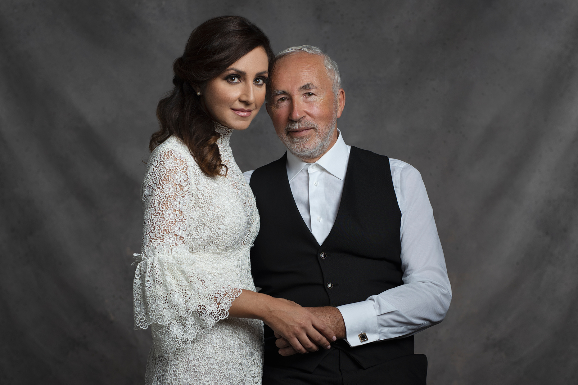 Fotografia fine art di padre e figlia in abiti da cerimonia, scattata da Claudia Spaziani nel suo studio a Bologna. Lei in abito bianco in pizzo con maniche a campana, lui in camicia bianca con gilet nero, mani intrecciate.padre