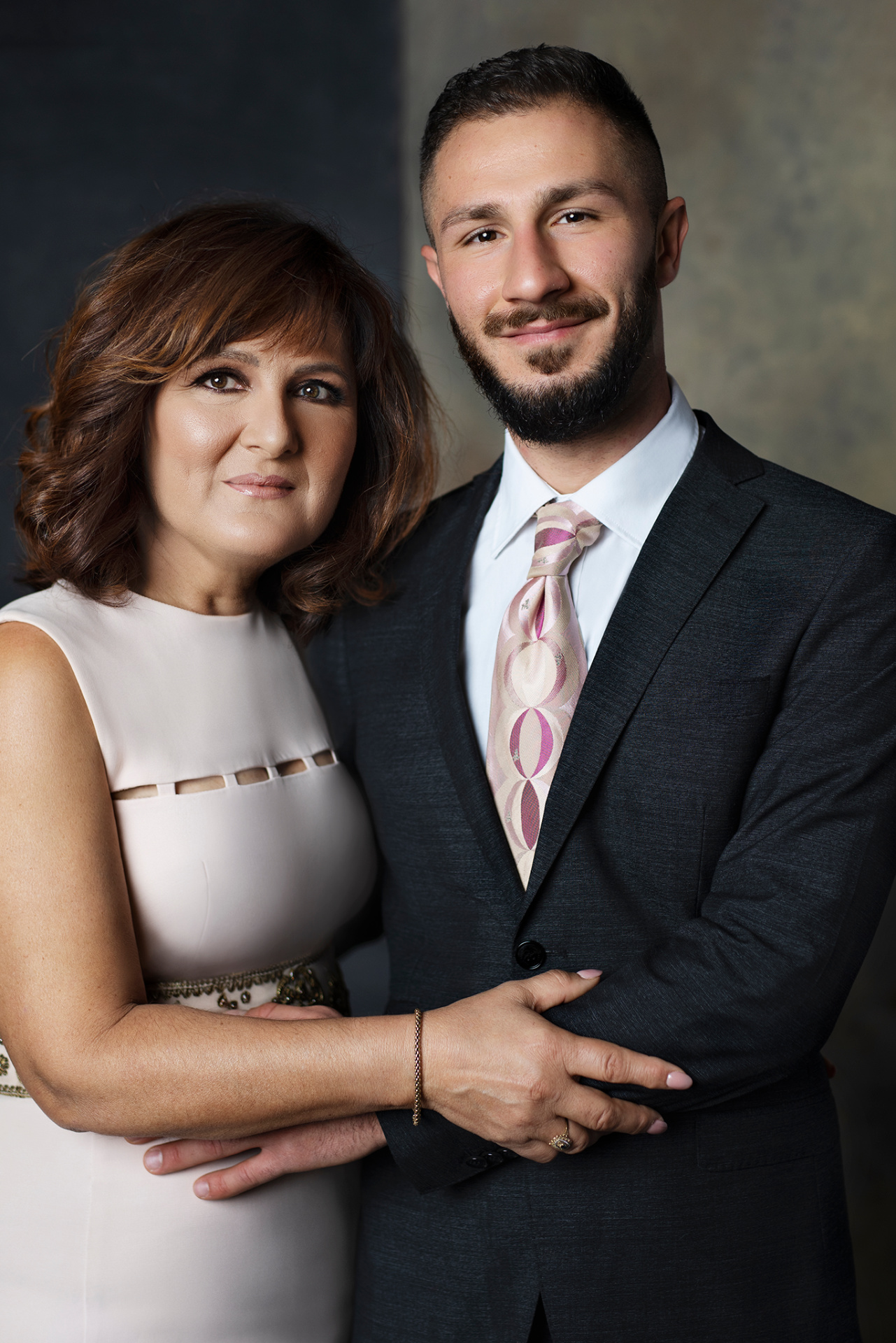 Fotografia fine art di madre e figlio in posa ravvicinata, scattata da Claudia Spaziani nel suo studio a Bologna. Lei in abito rosa cipria con dettagli decorativi, lui in completo scuro con cravatta a motivi rosa e beige.