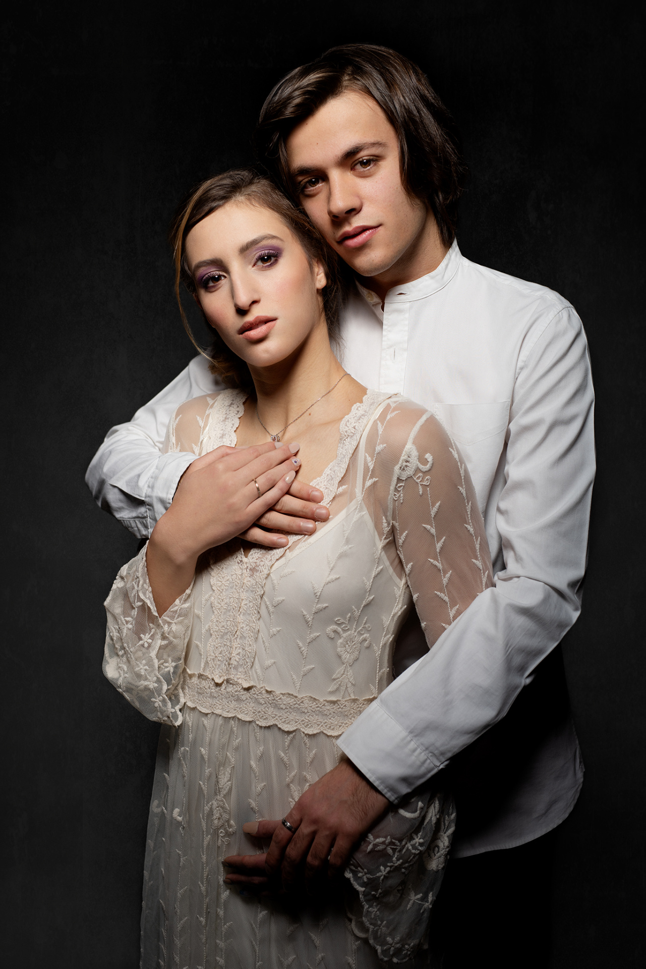 Fotografia artistica di una coppia in abiti chiari, uno con camicia bianca e l’altro con vestito ricamato. Scatto realizzato da Claudia Spaziani nel suo studio a Bologna, con sfondo scuro e composizione che esprime amore e dolcezza.