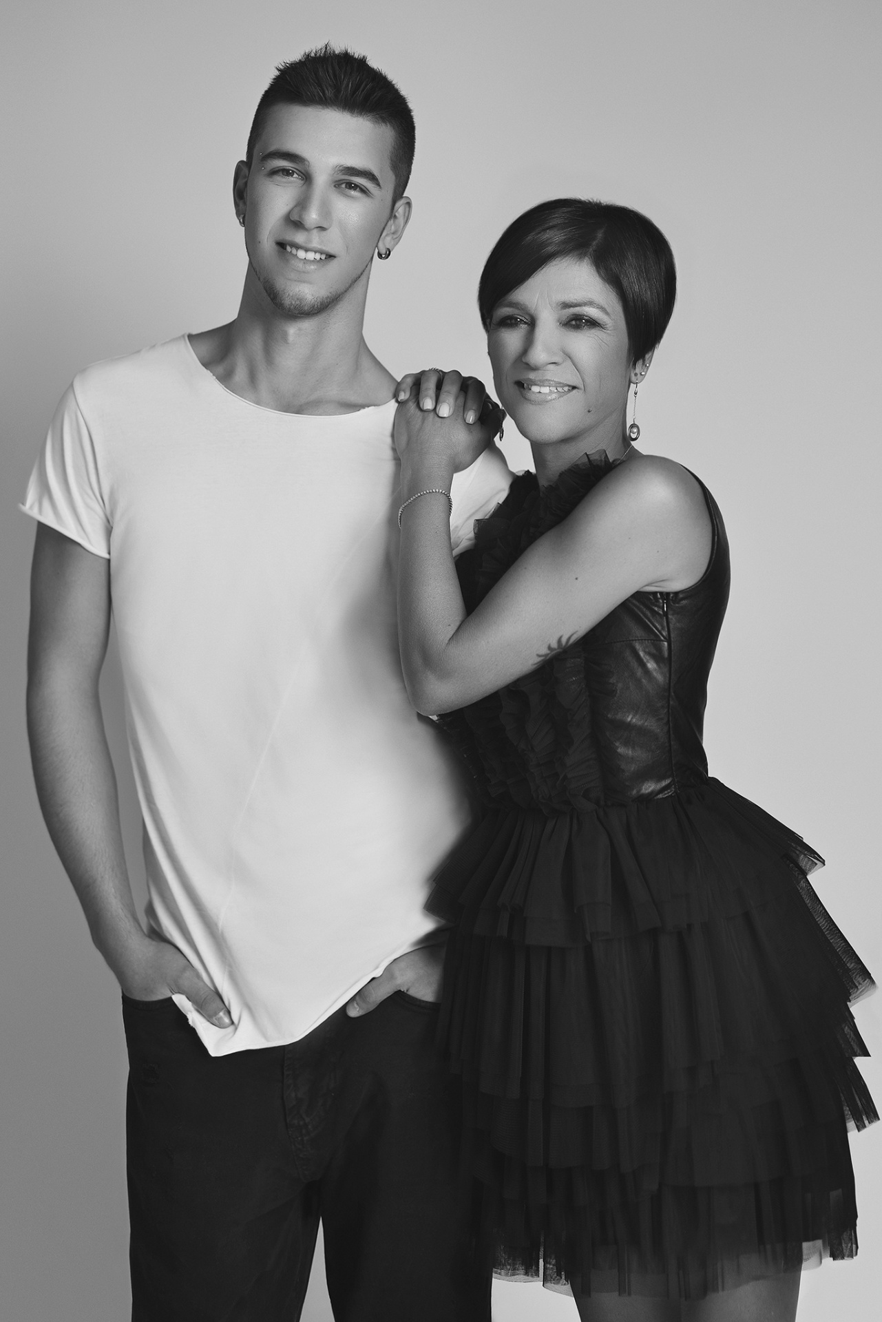 Madre in abito nero con tulle e figlio in t‑shirt bianca posano insieme sorridendo, in uno scatto fine art monocromatico realizzato da Claudia Spaziani nel suo studio a Bologna.