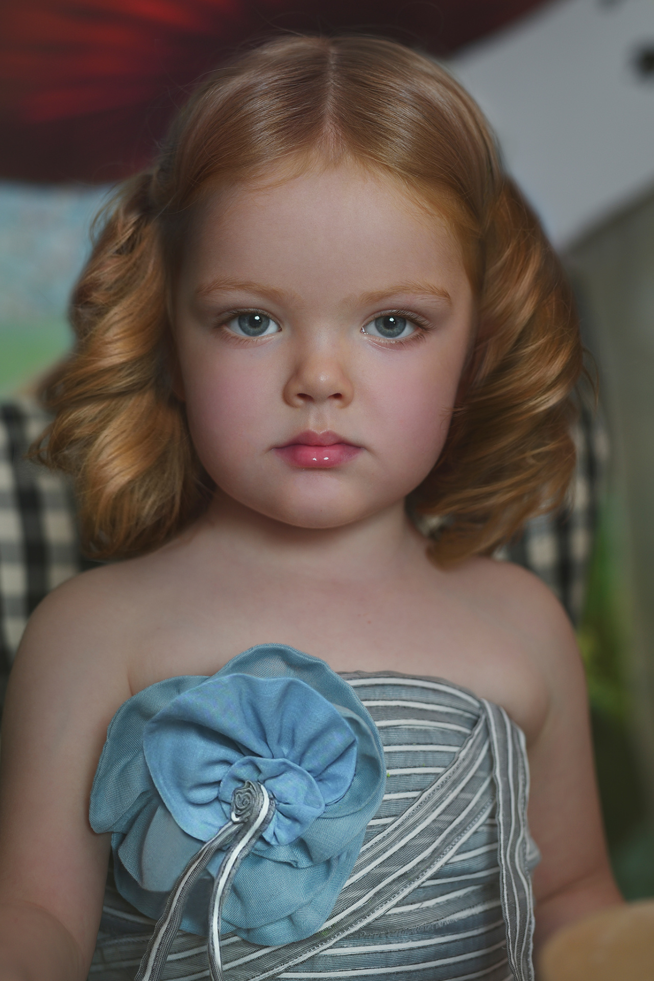 Ritratto creativo di bambina con fiocco blu e abito a righe, ambientato in un set decorativo ispirato a Alice in Wonderland.