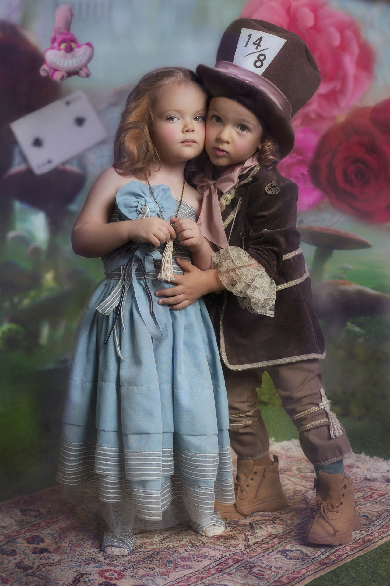 Ritratto teatrale con bambini in abiti da fiaba, ambientato in un set magico con fiori giganti e personaggi di Alice.