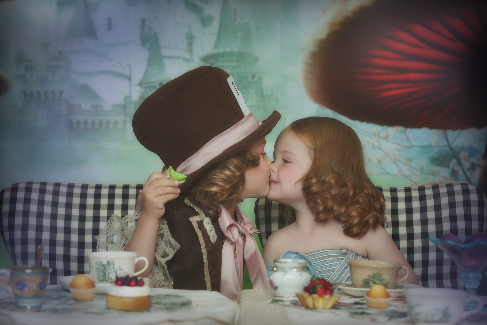 Ritratto emozionale di due bambini che si baciano in costume fantasy, ambientato in un set ispirato a Wonderland nello studio di Bologna.