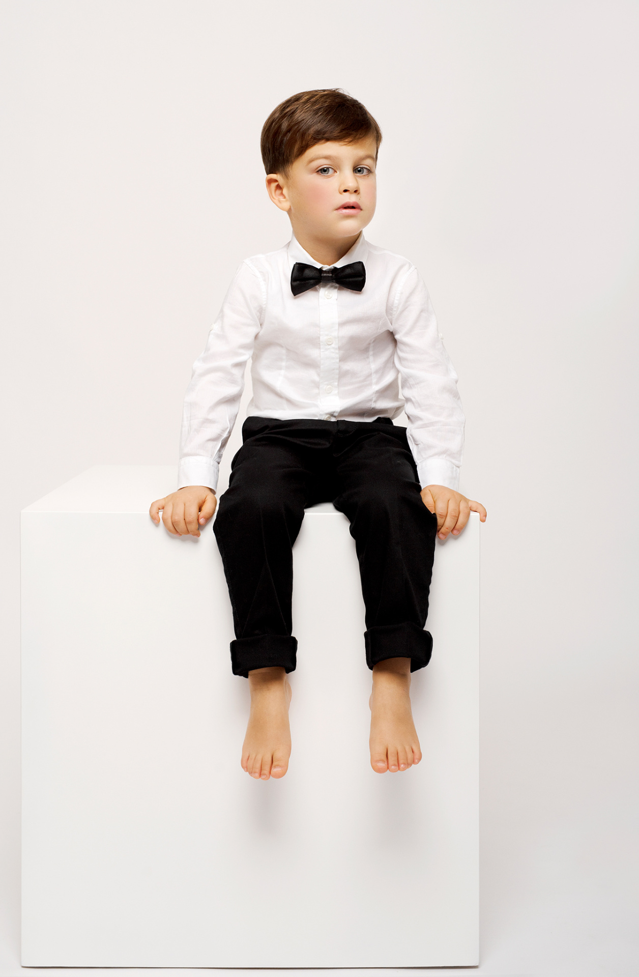 Ritratto pulito di bambino in camicia bianca con papillon e pantaloni neri, su sfondo bianco, scattato da Claudia Spaziani nel suo studio fotografico a Bologna.