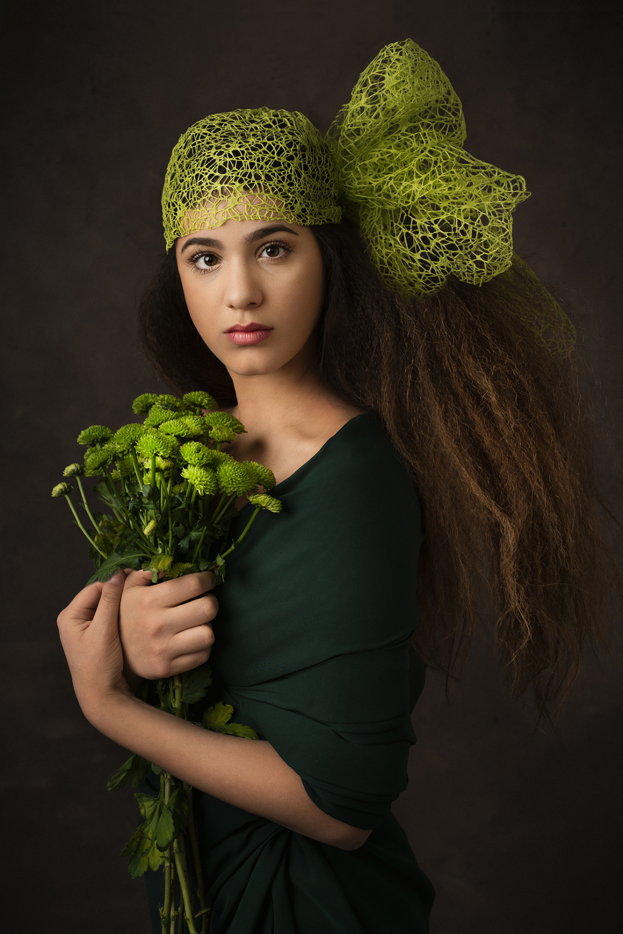 Ritratto artistico di adolescente in abito verde con bouquet di crisantemi e copricapo in rete, scattato da Claudia Spaziani nel suo studio fotografico a Bologna.