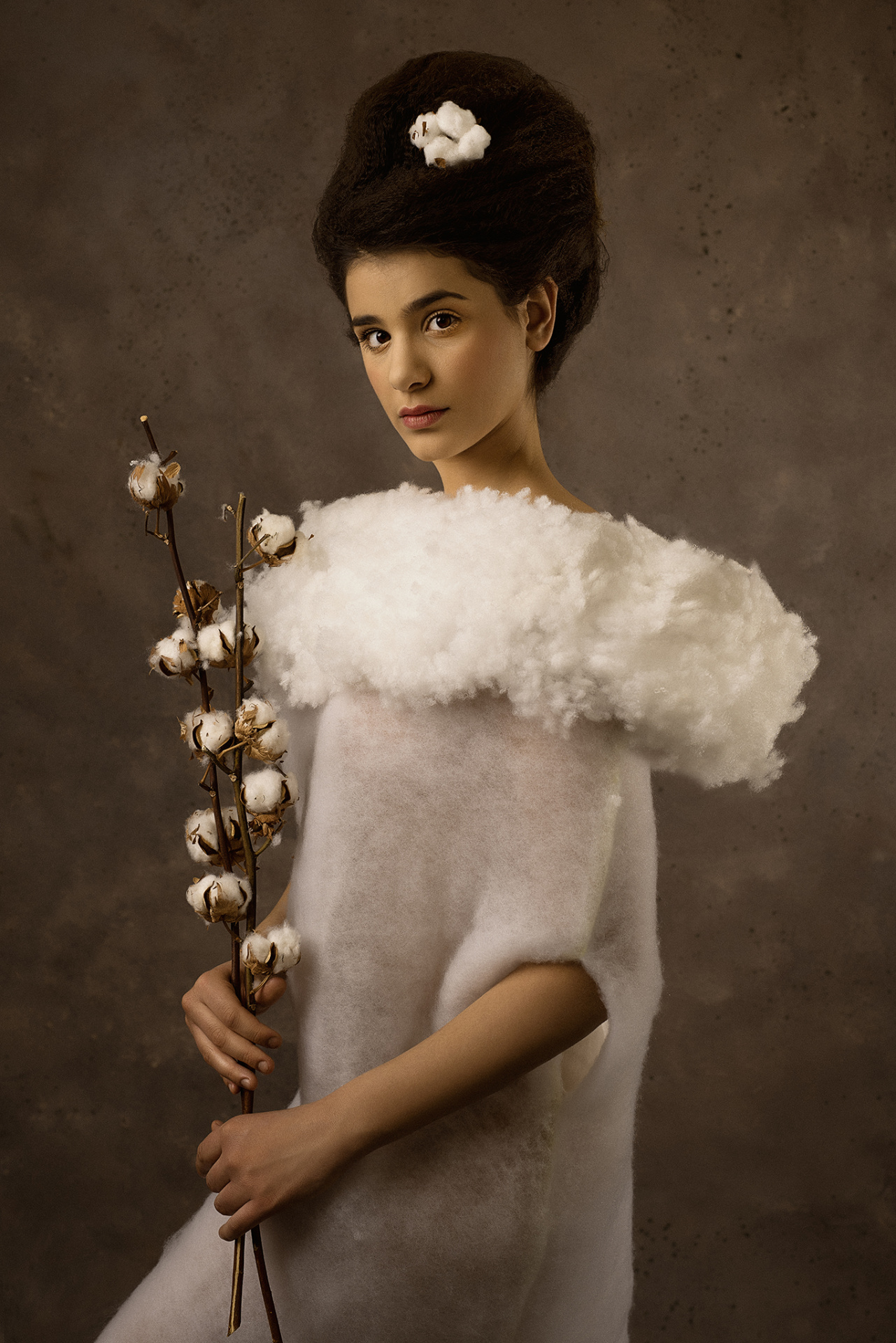 Ritratto evocativo di adolescente con ramo di cotone e acconciatura decorata, su sfondo neutro, realizzato da Claudia Spaziani a Bologna.