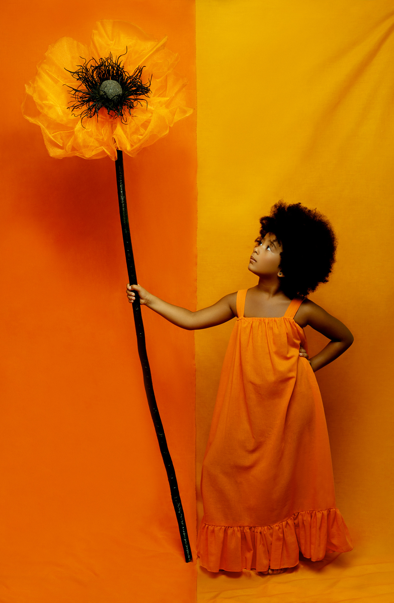 Ritratto artistico di bambina in abito arancione con fiore oversize, su sfondo bicolore, realizzato da Claudia Spaziani a Bologna.
