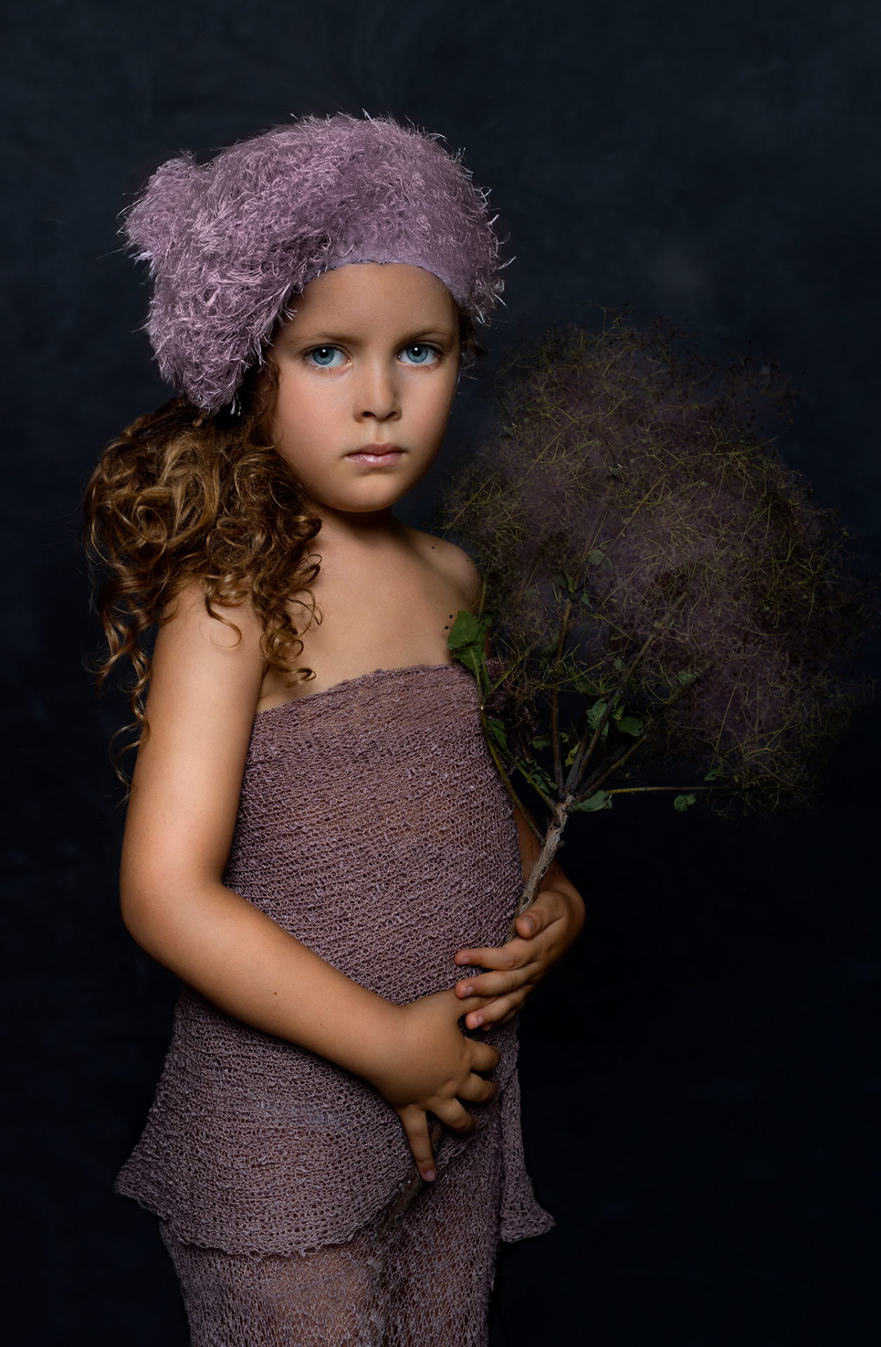Ritratto fine-art di bambina con abito testurizzato e berretto lavanda, su sfondo scuro, realizzato da Claudia Spaziani nel suo studio fotografico a Bologna.
