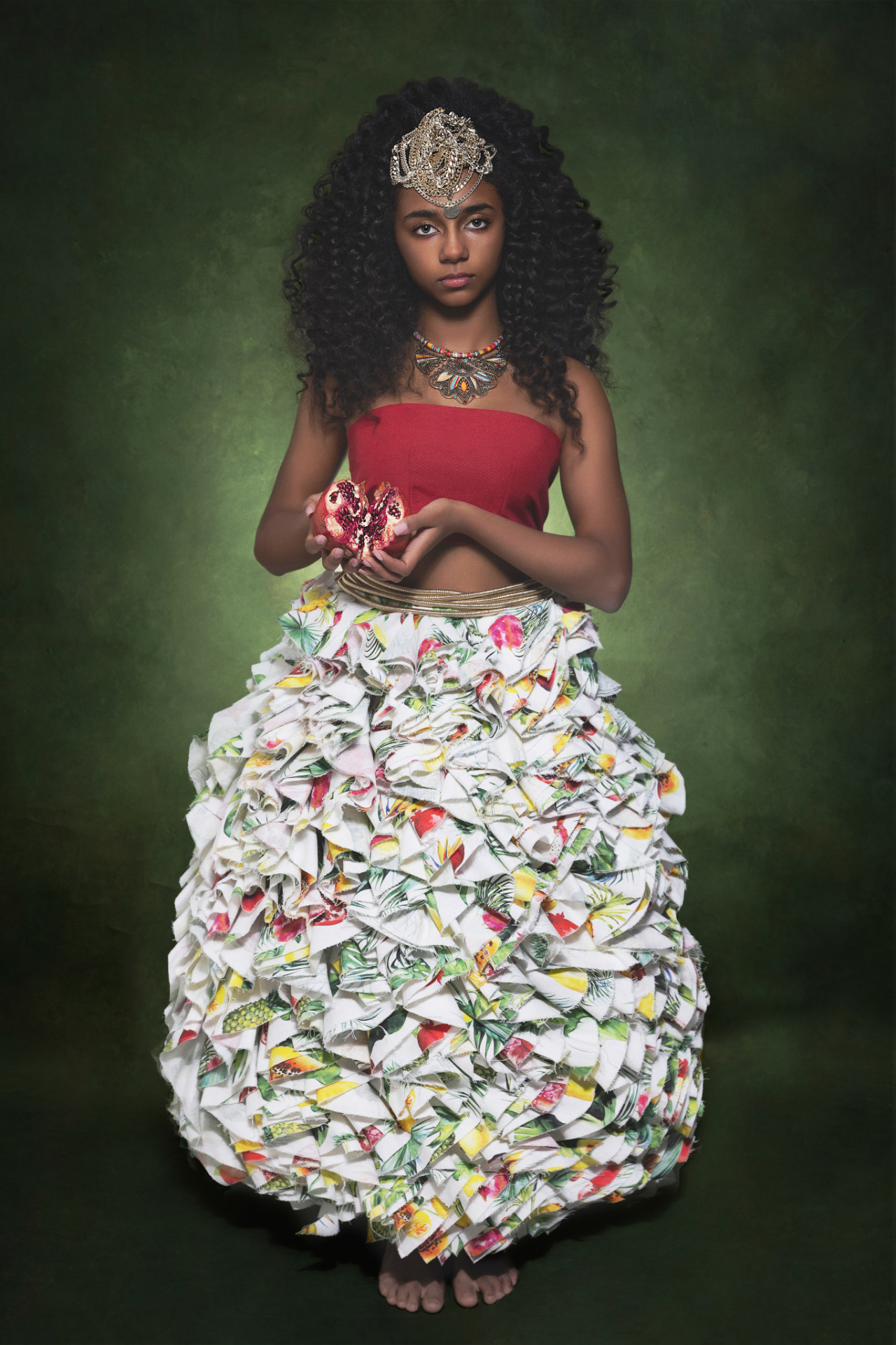 Ritratto evocativo di adolescente in abito tropicale con melagrana tra le mani e copricapo gioiello, realizzato da Claudia Spaziani nel suo studio fotografico a Bologna.