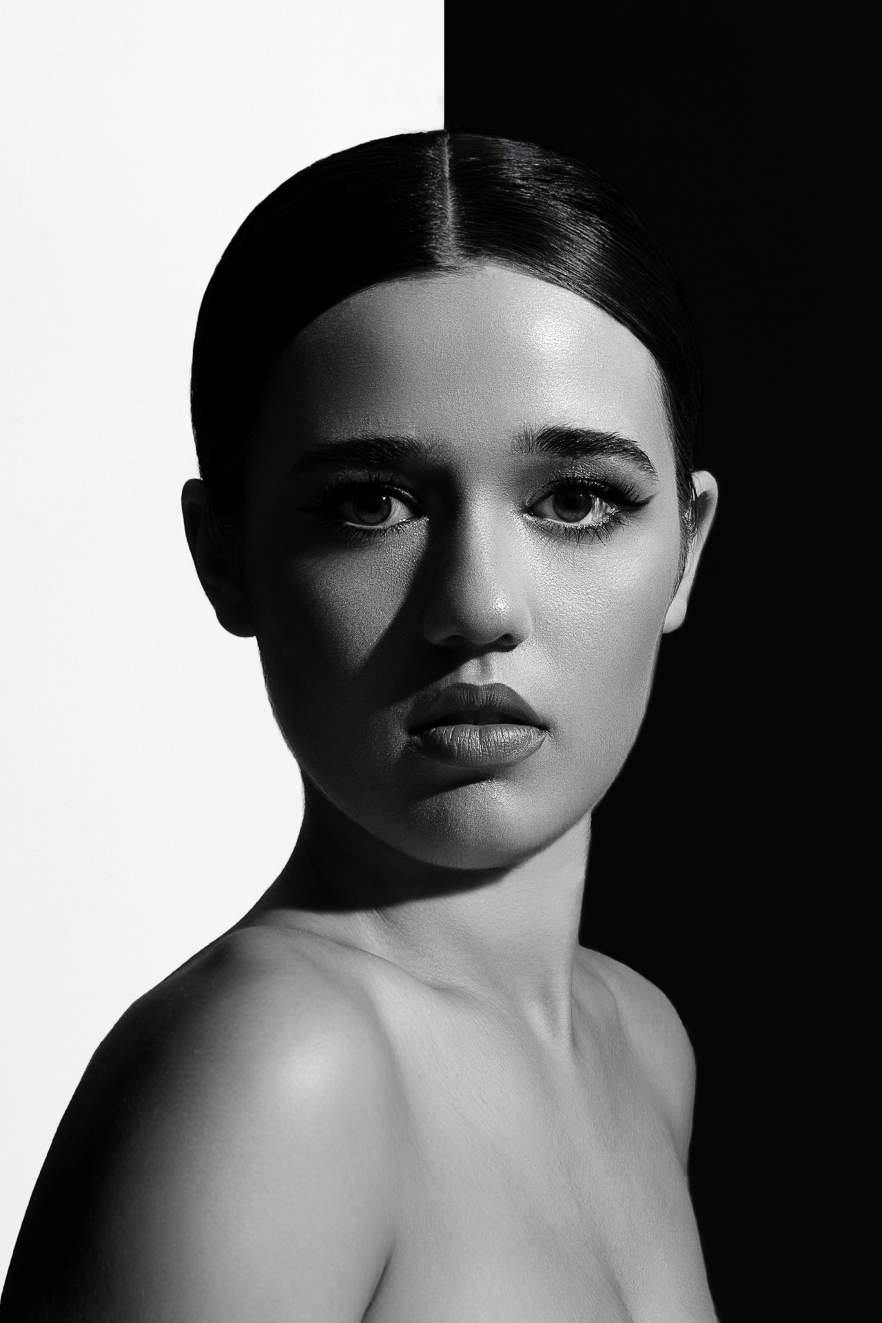 Ritratto in bianco e nero di adolescente con capelli raccolti, illuminazione drammatica e sfondo diviso, scattato da Claudia Spaziani nel suo studio fotografico a Bologna.
